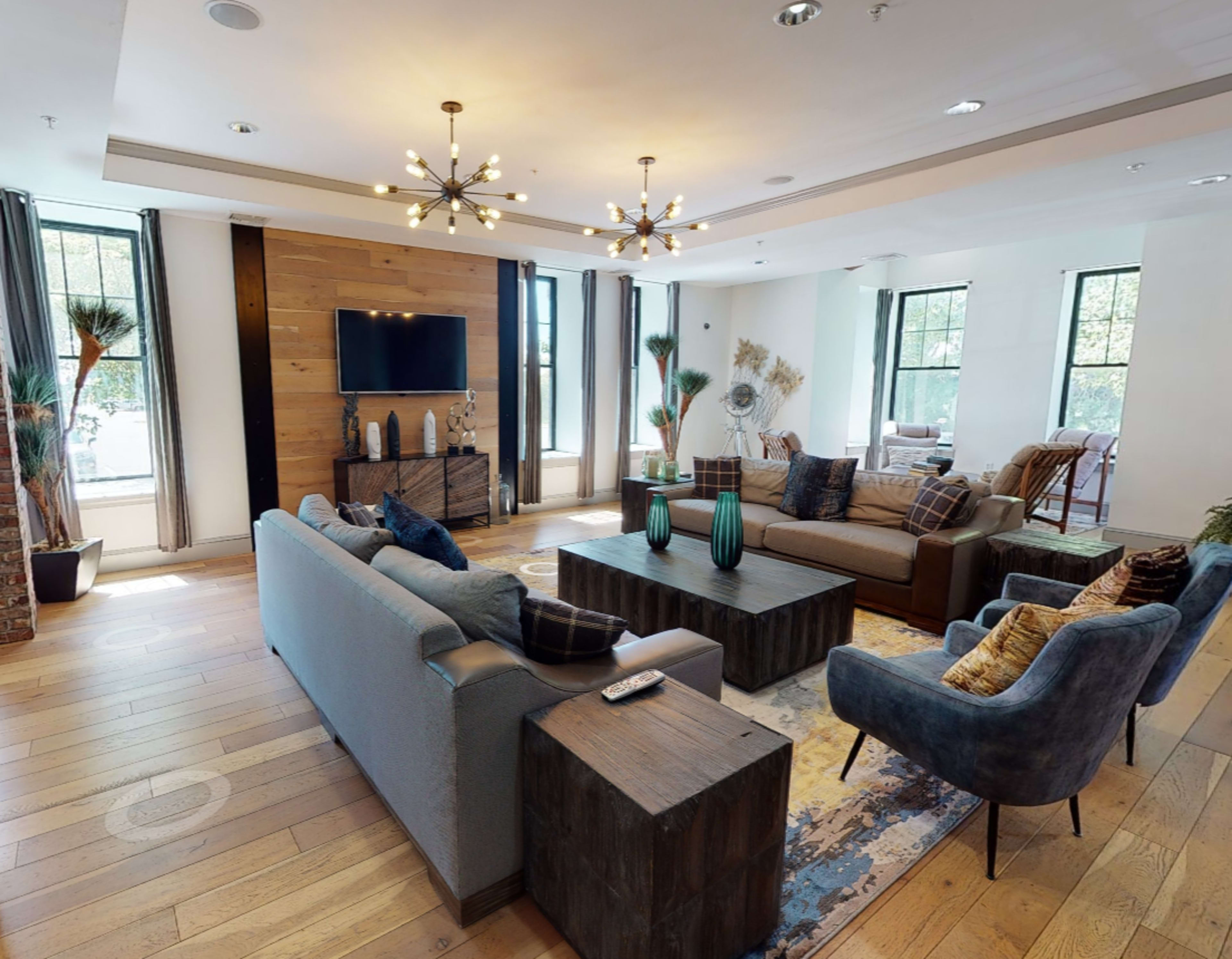 A modern living room features a large coffee table, comfortable seating areas, and windows with natural light.
