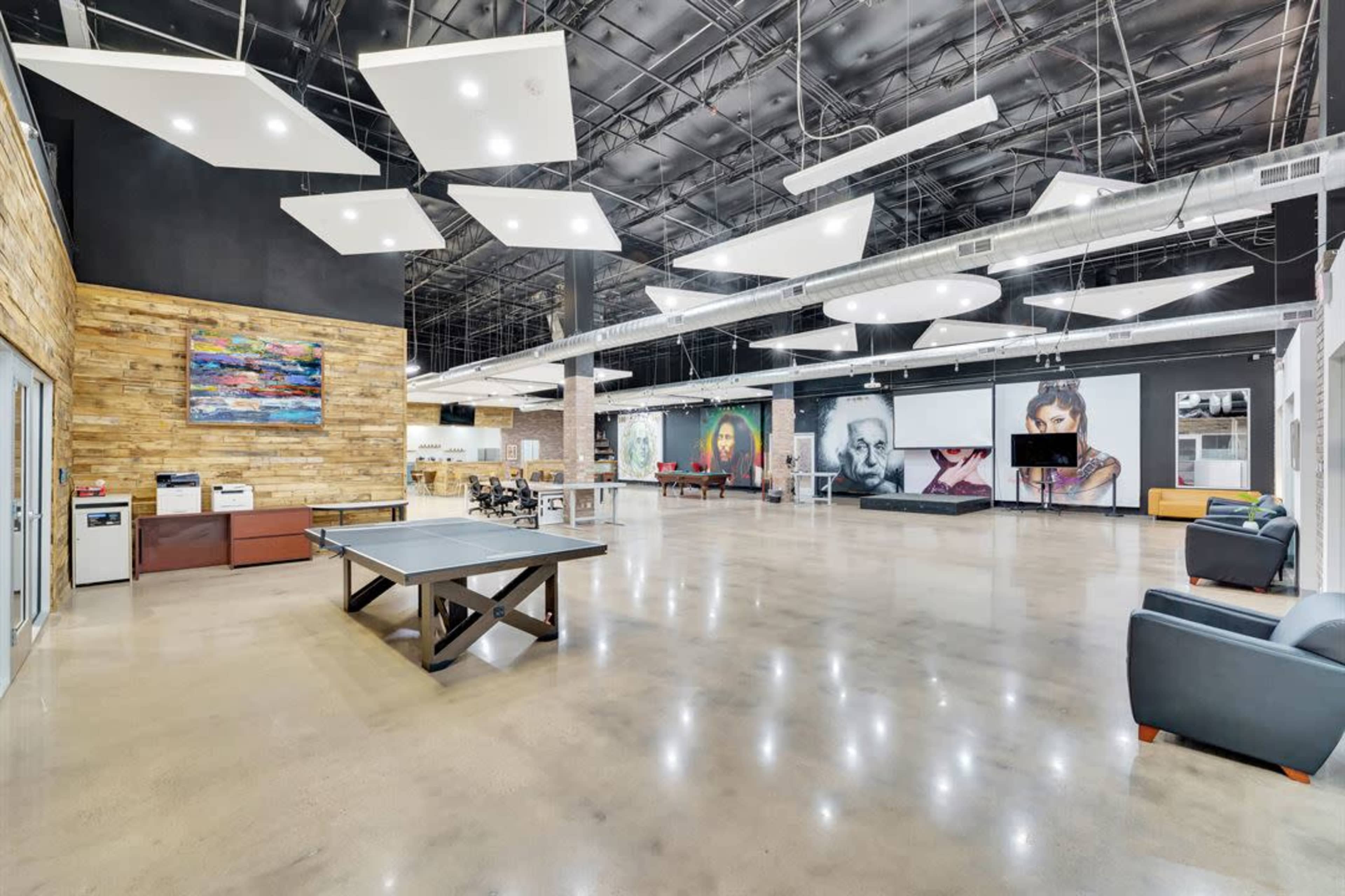 A spacious and modern open area featuring a ping pong table, lounge seating, and large wall art.