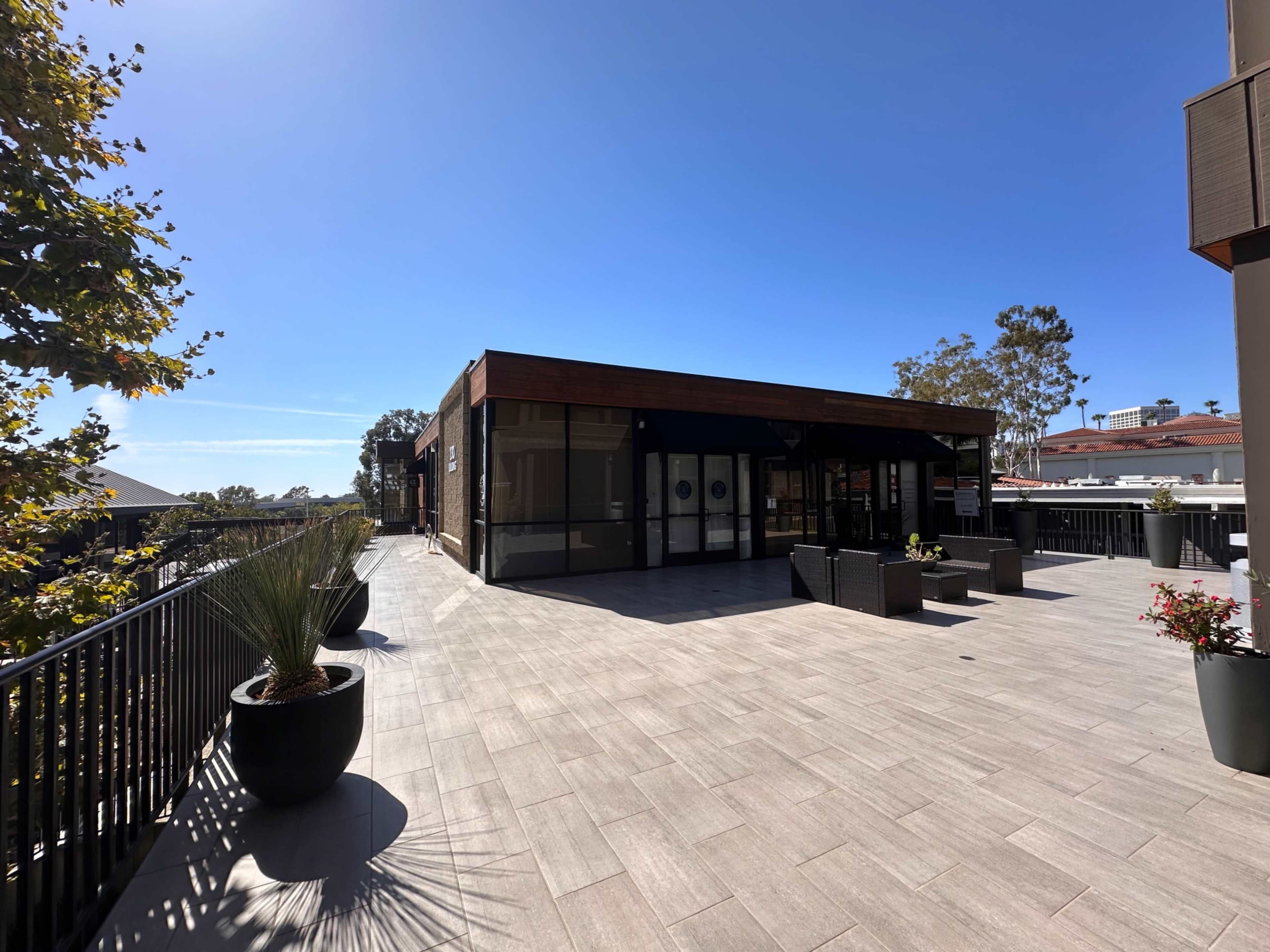 A modern terrace features a seating area with planters and overlooks a clear blue sky.