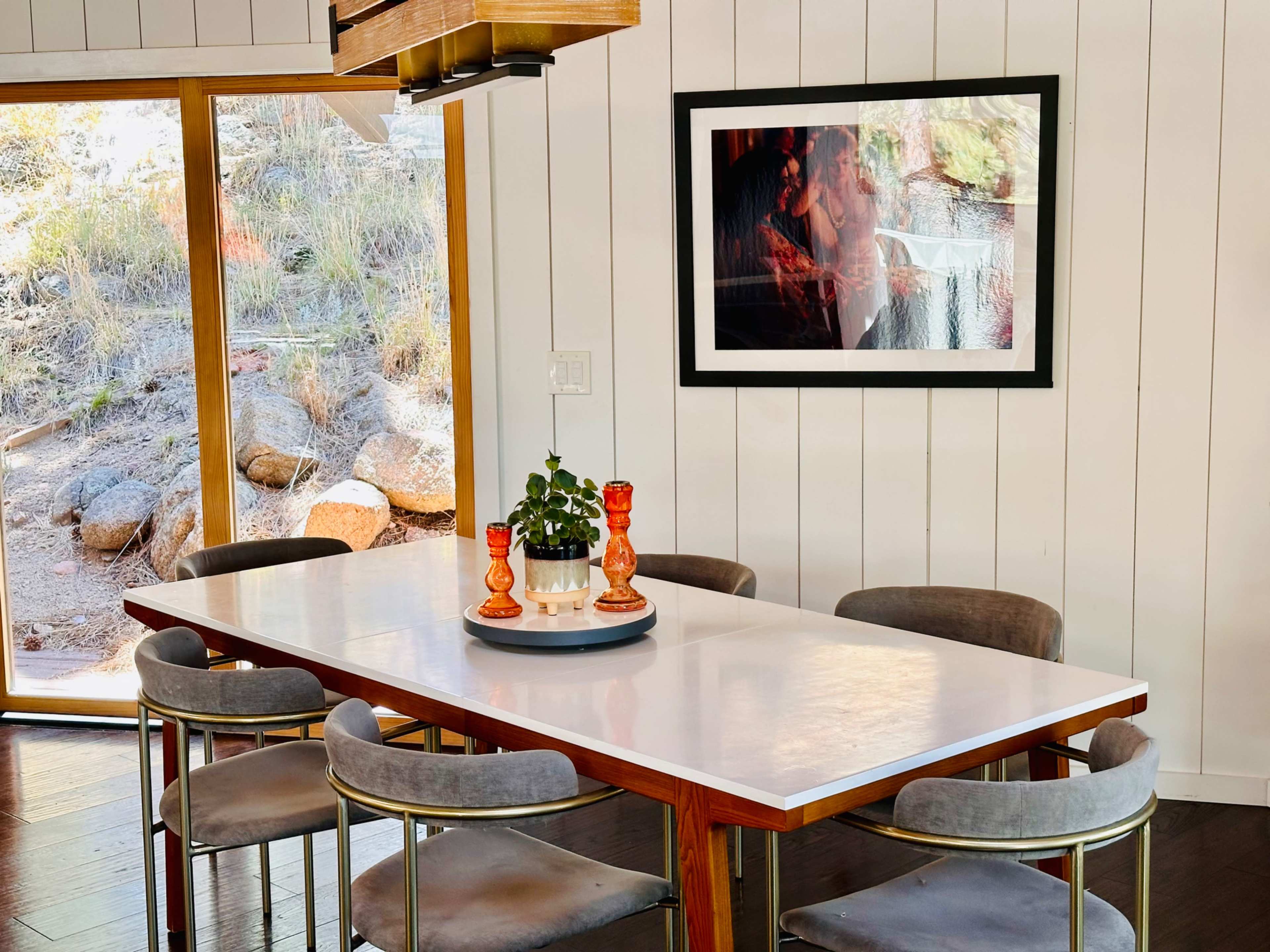 A dining table with eight chairs is positioned in a room featuring a large window and a framed photograph on the wall.