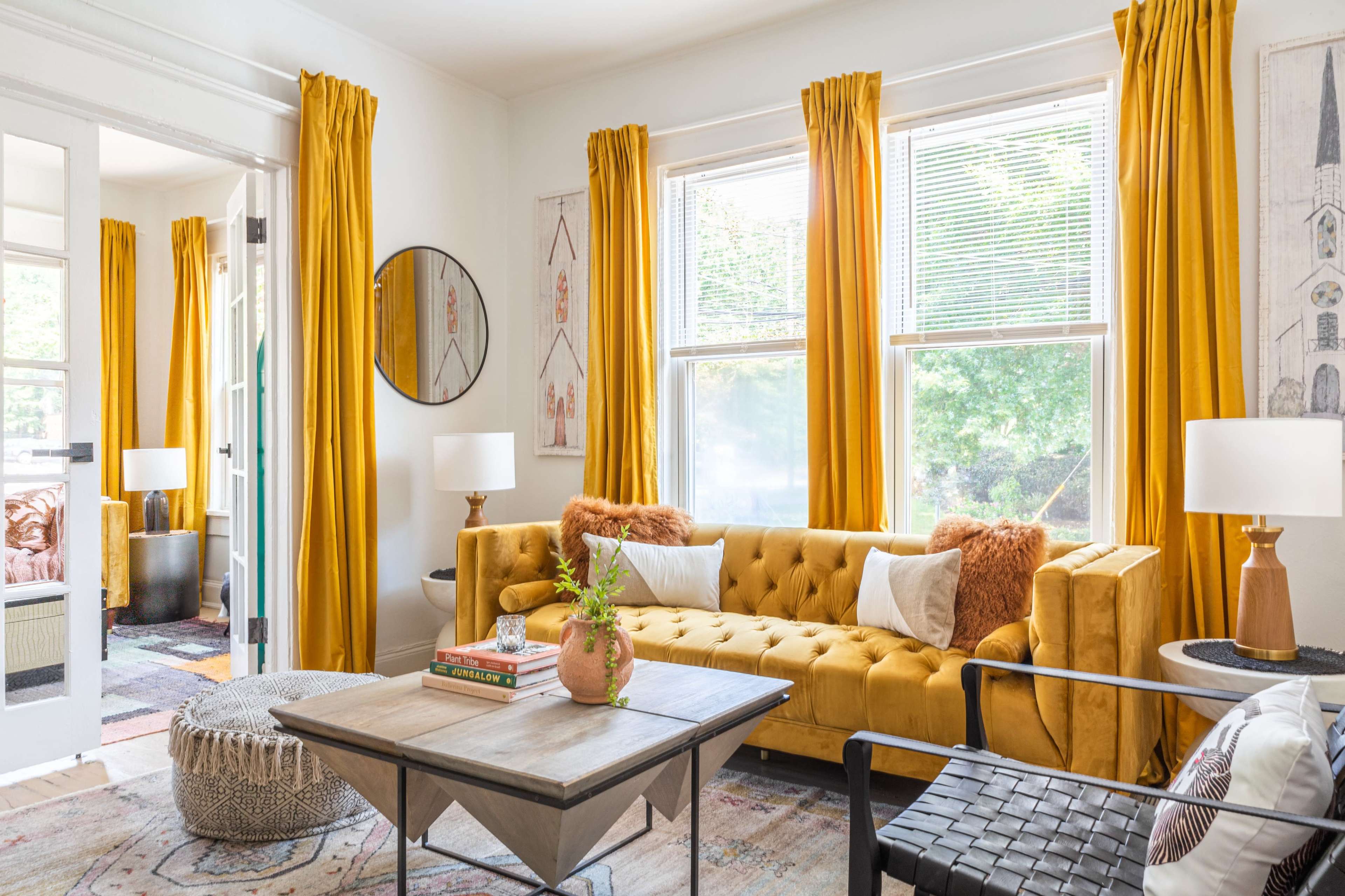 The scene features a bright living room with a yellow tufted sofa, wooden coffee table, and large windows dressed in matching yellow curtains.