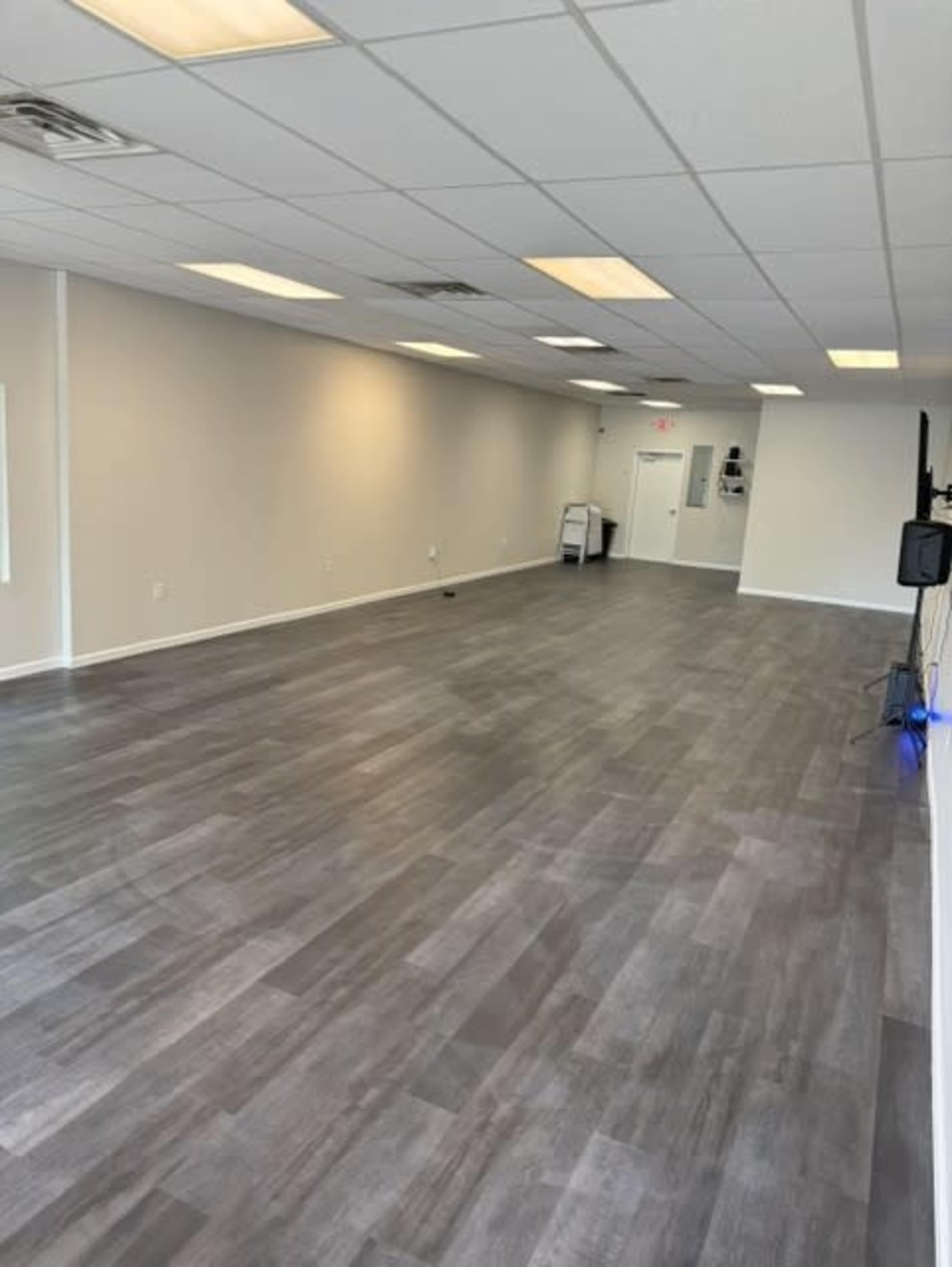 The image shows an empty room with gray flooring, white walls, and fluorescent lighting.