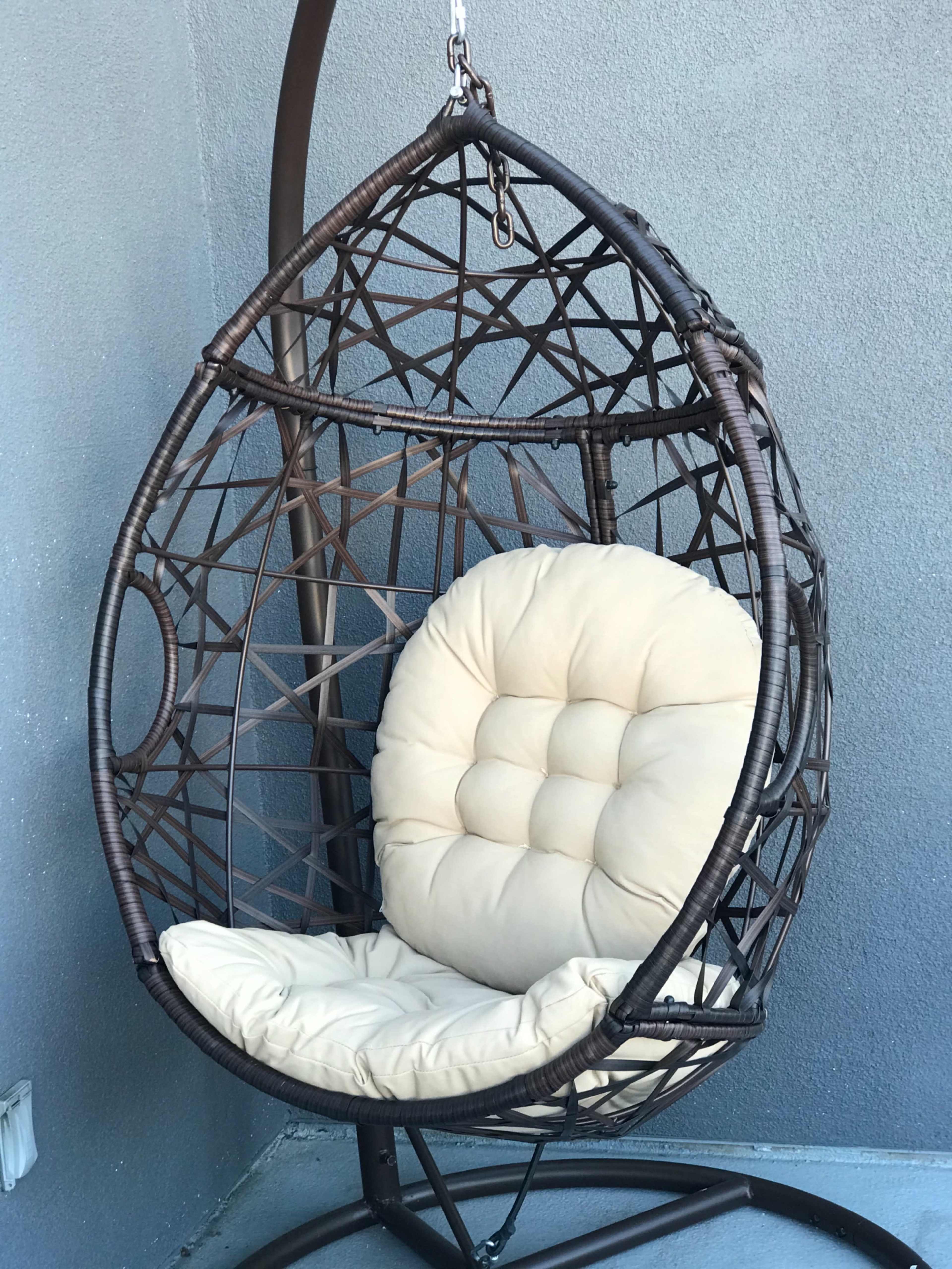 A hanging egg-shaped chair made of woven material with a cream-colored cushion.