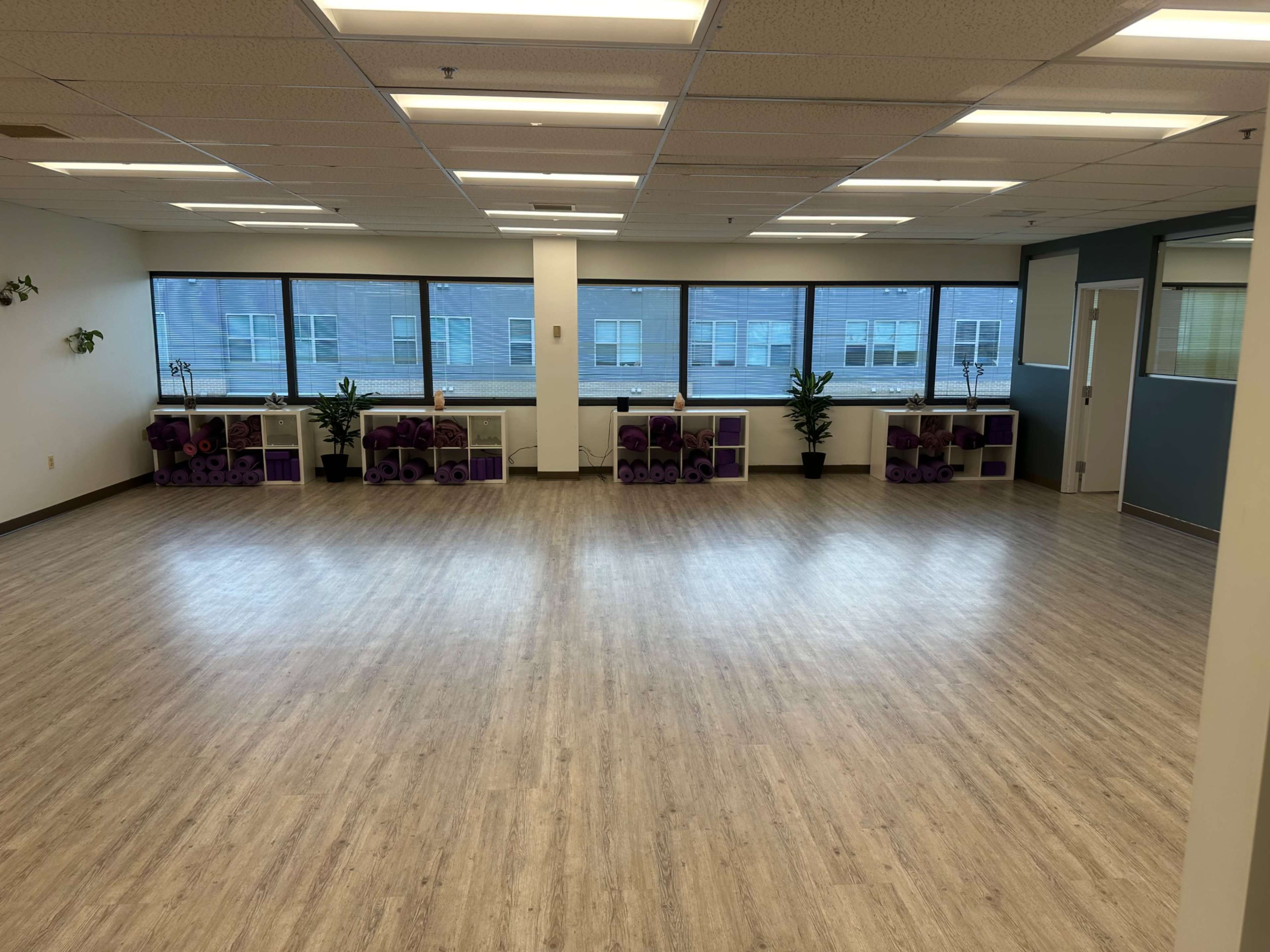 A spacious, empty room with large windows and shelves holding yoga mats.