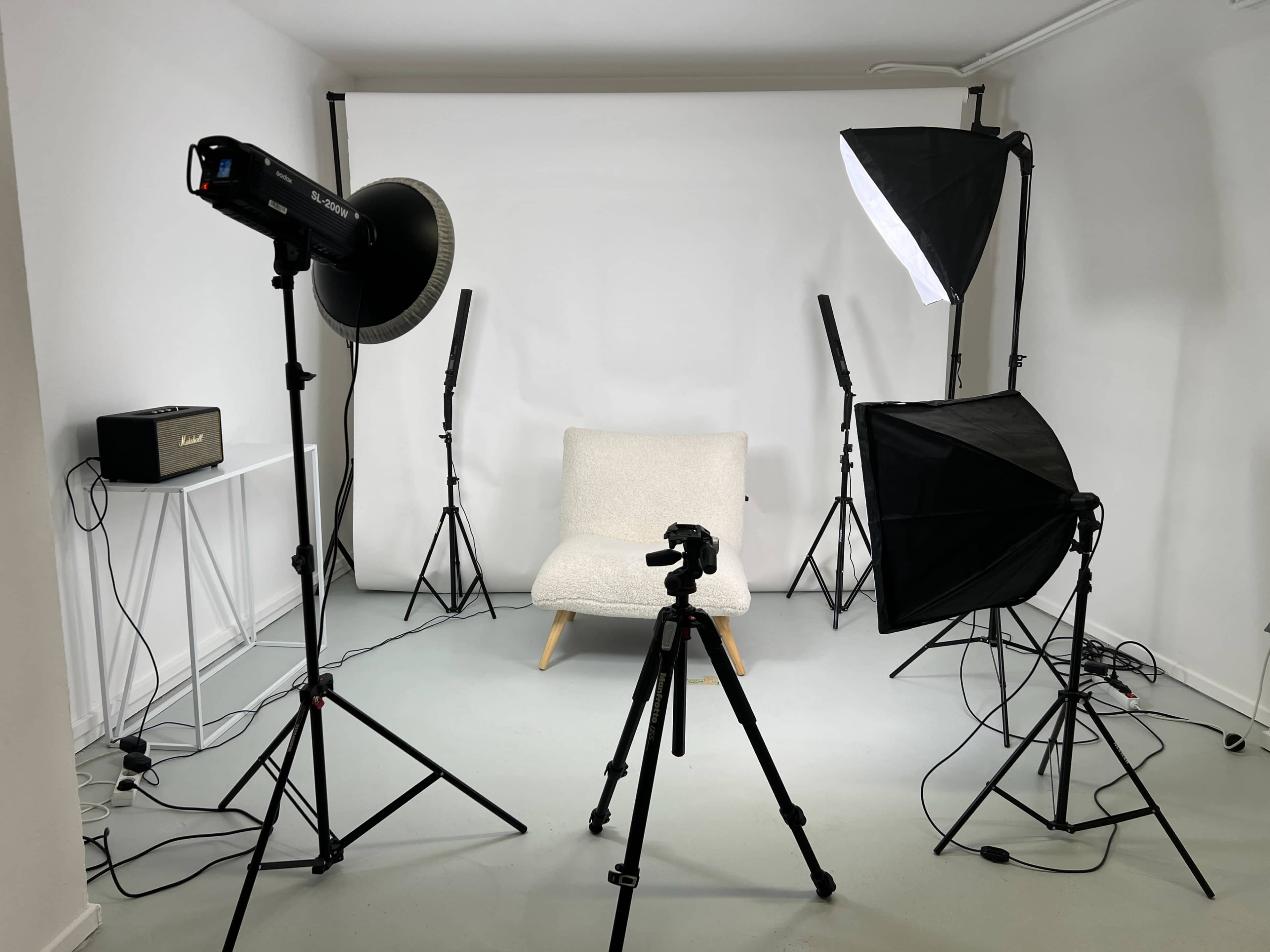 A photography studio setup features a light gray background, a chair in the center, and multiple lighting equipment arranged around it.