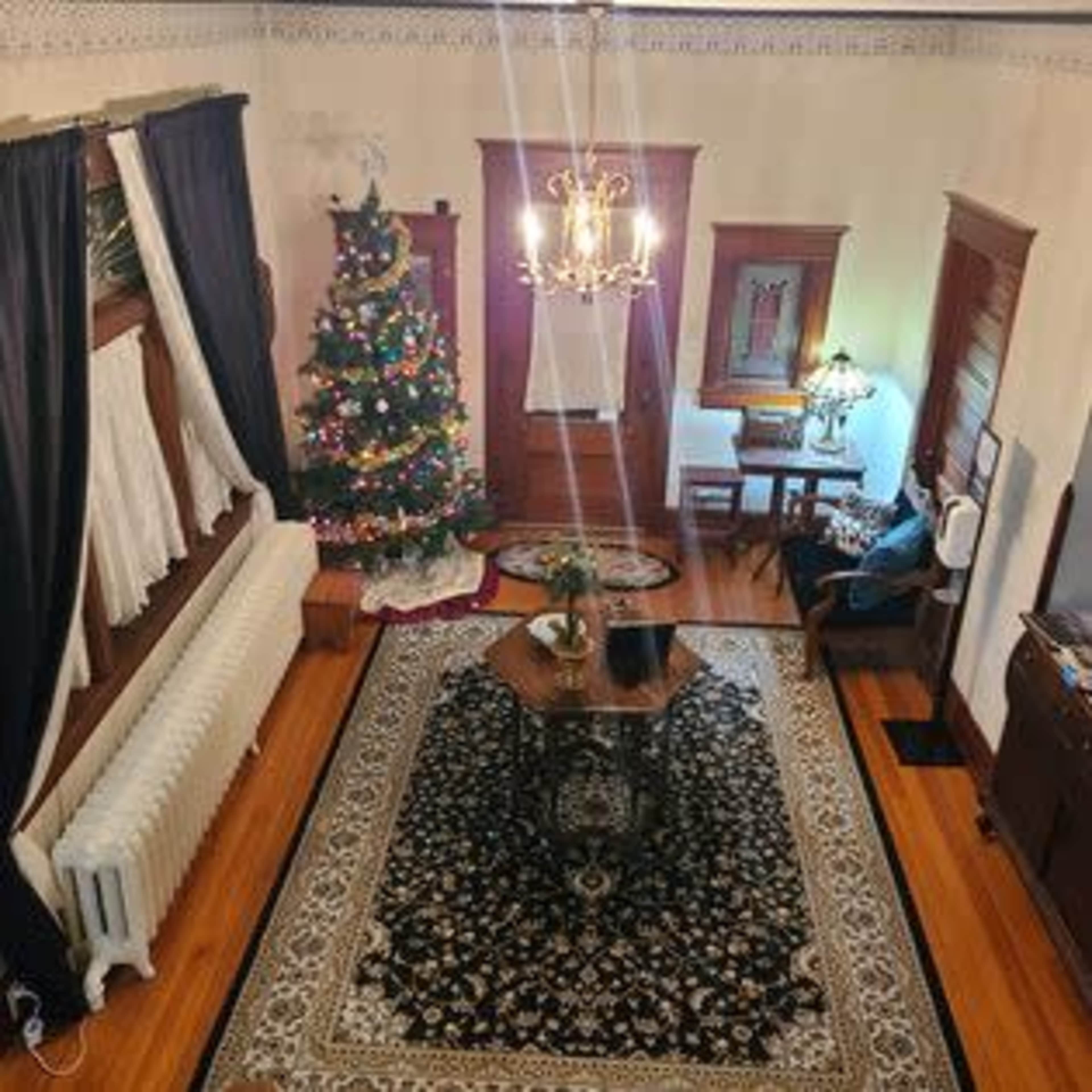 The image shows a warmly decorated living room featuring a Christmas tree, a large patterned rug, and wooden furniture.