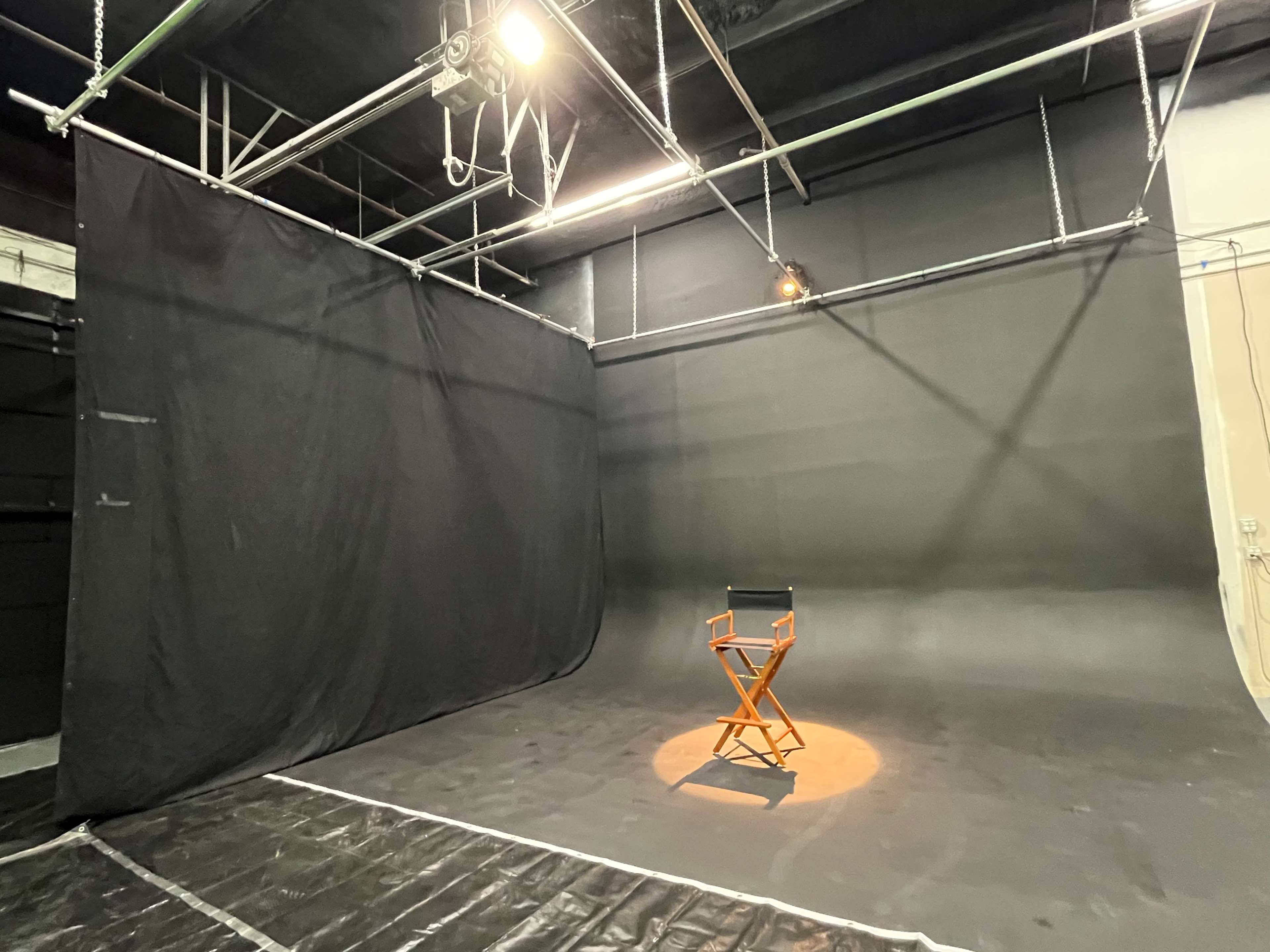 A sparsely decorated studio space with a folding director's chair placed on a lit section of a dark backdrop.