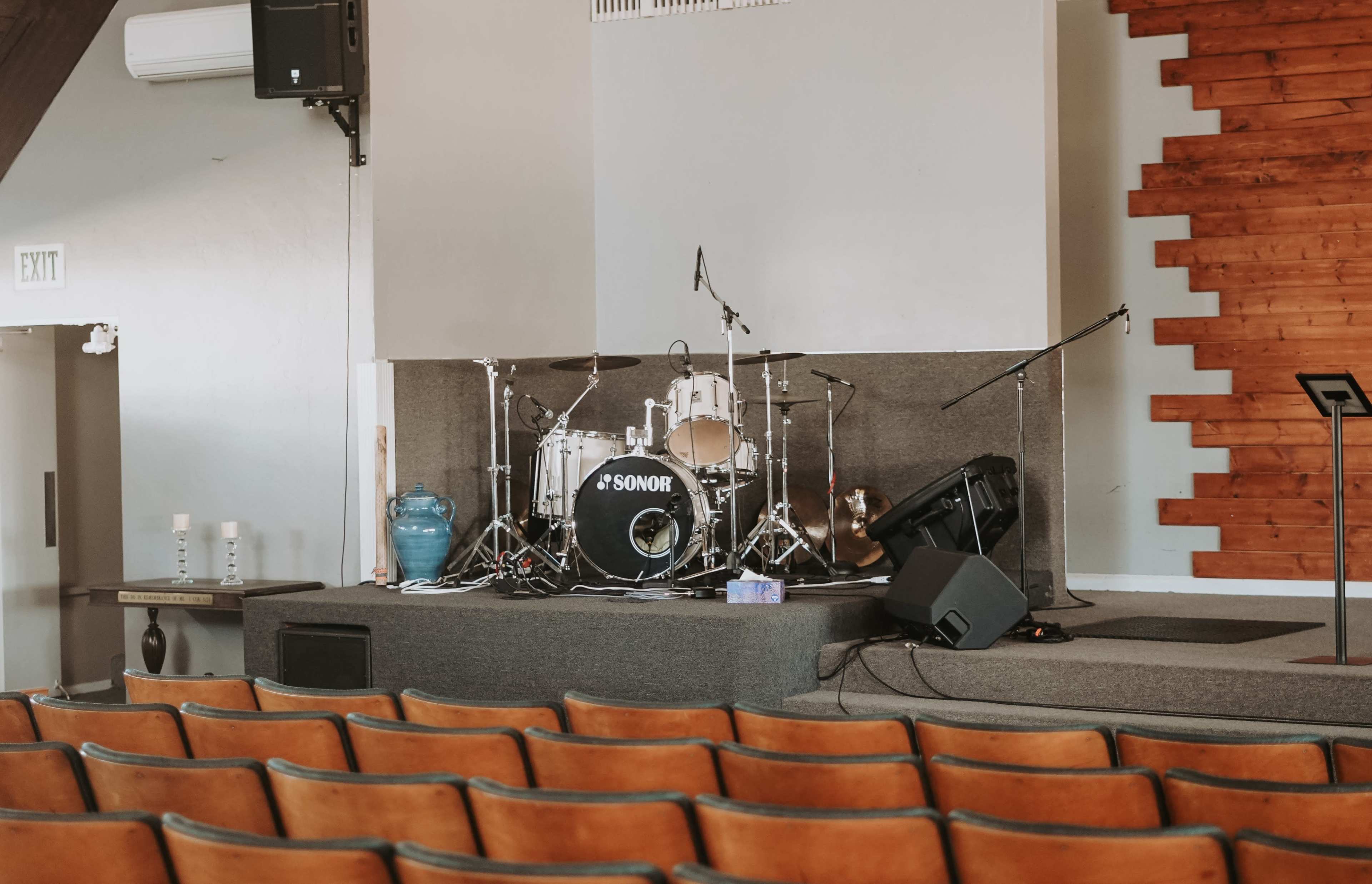 A stage with a drum set and microphones, accompanied by empty rows of brown seats in a music venue.