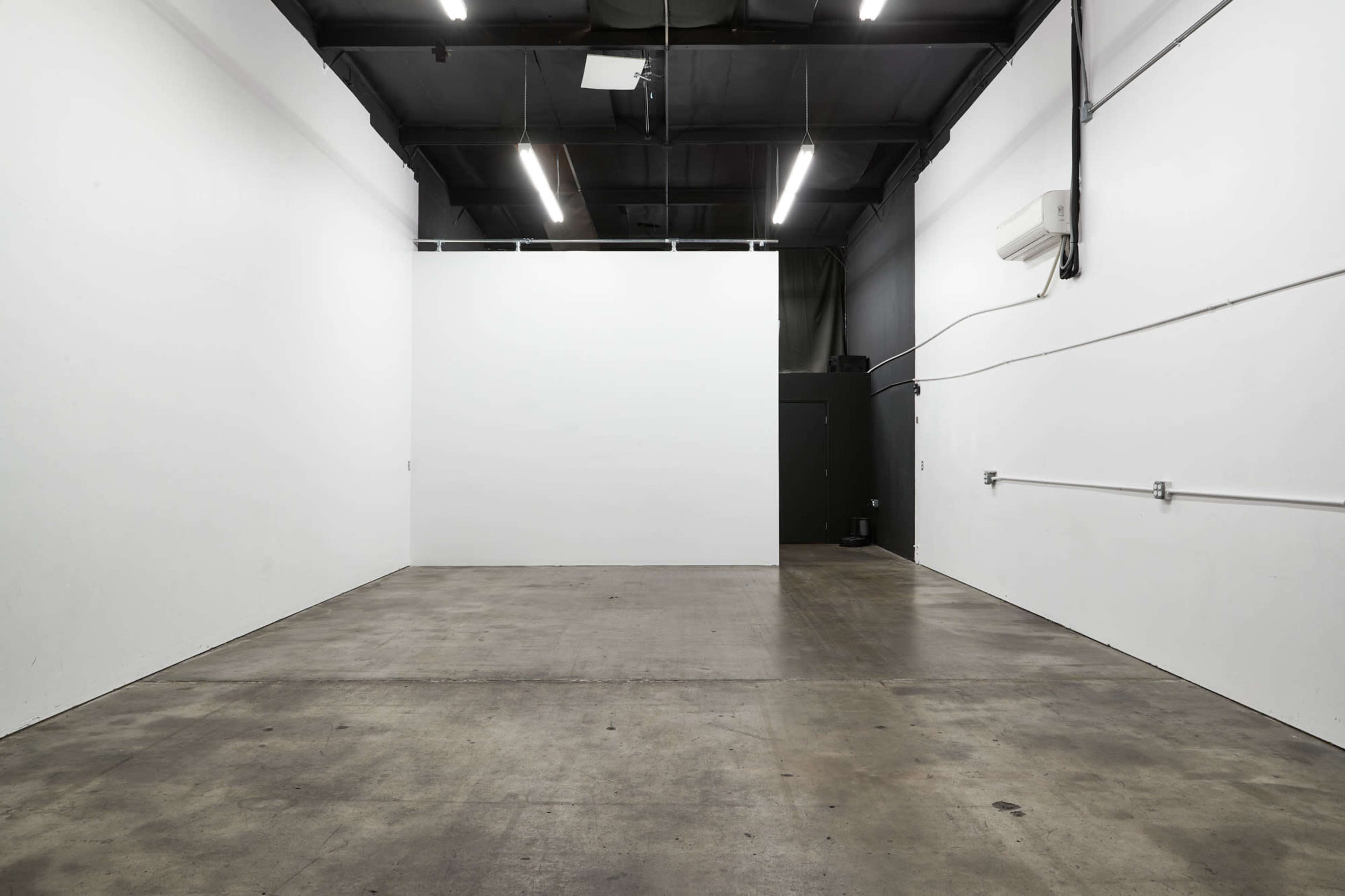 An empty room with concrete flooring, white walls, and overhead fluorescent lights.