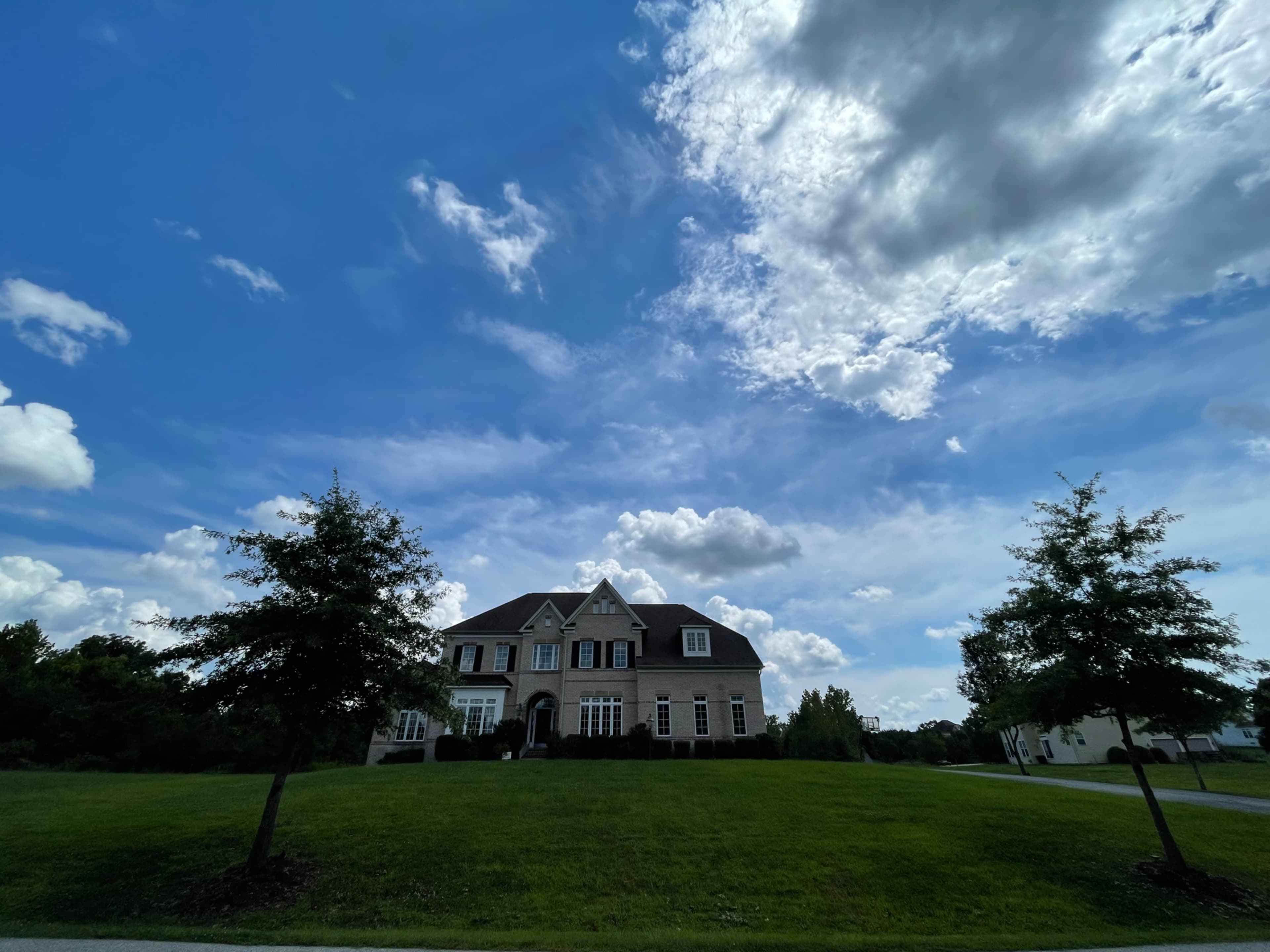 A large two-story house with a manicured lawn is set against a backdrop of blue sky and scattered clouds.