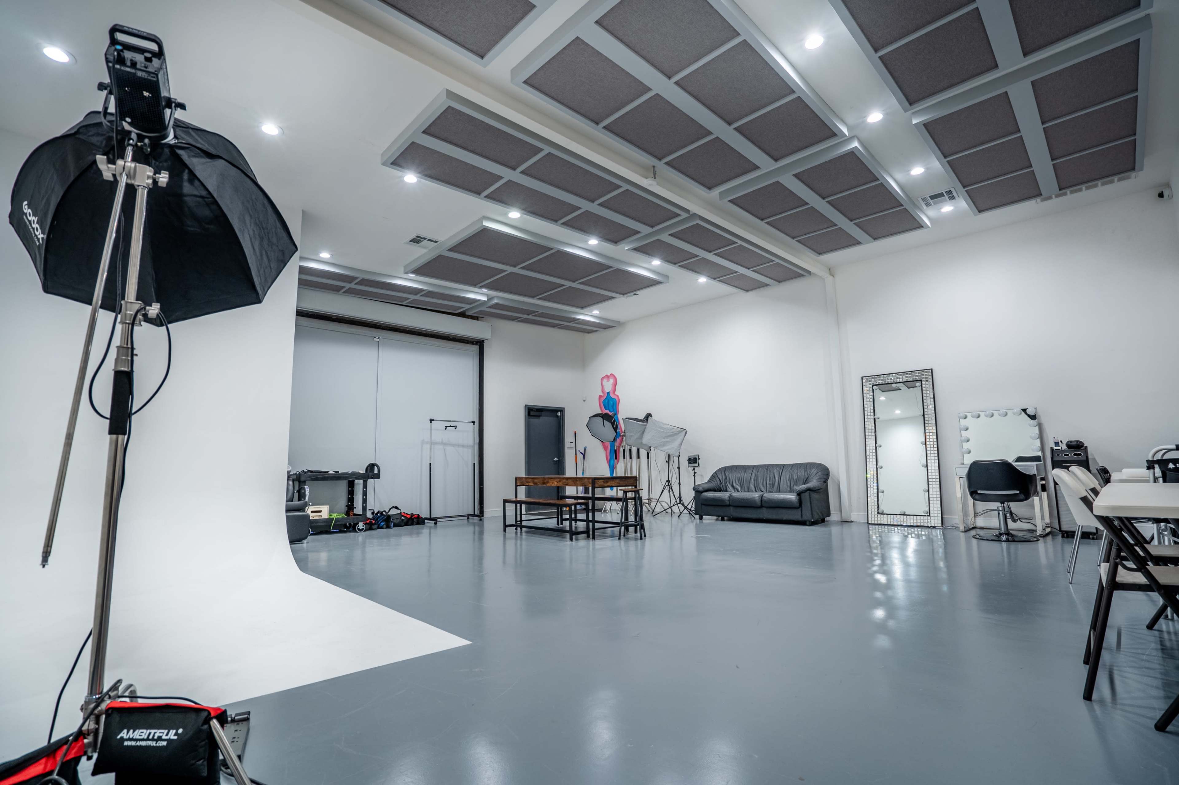 The image shows a spacious photography studio featuring a white backdrop, furniture, and various photography equipment.