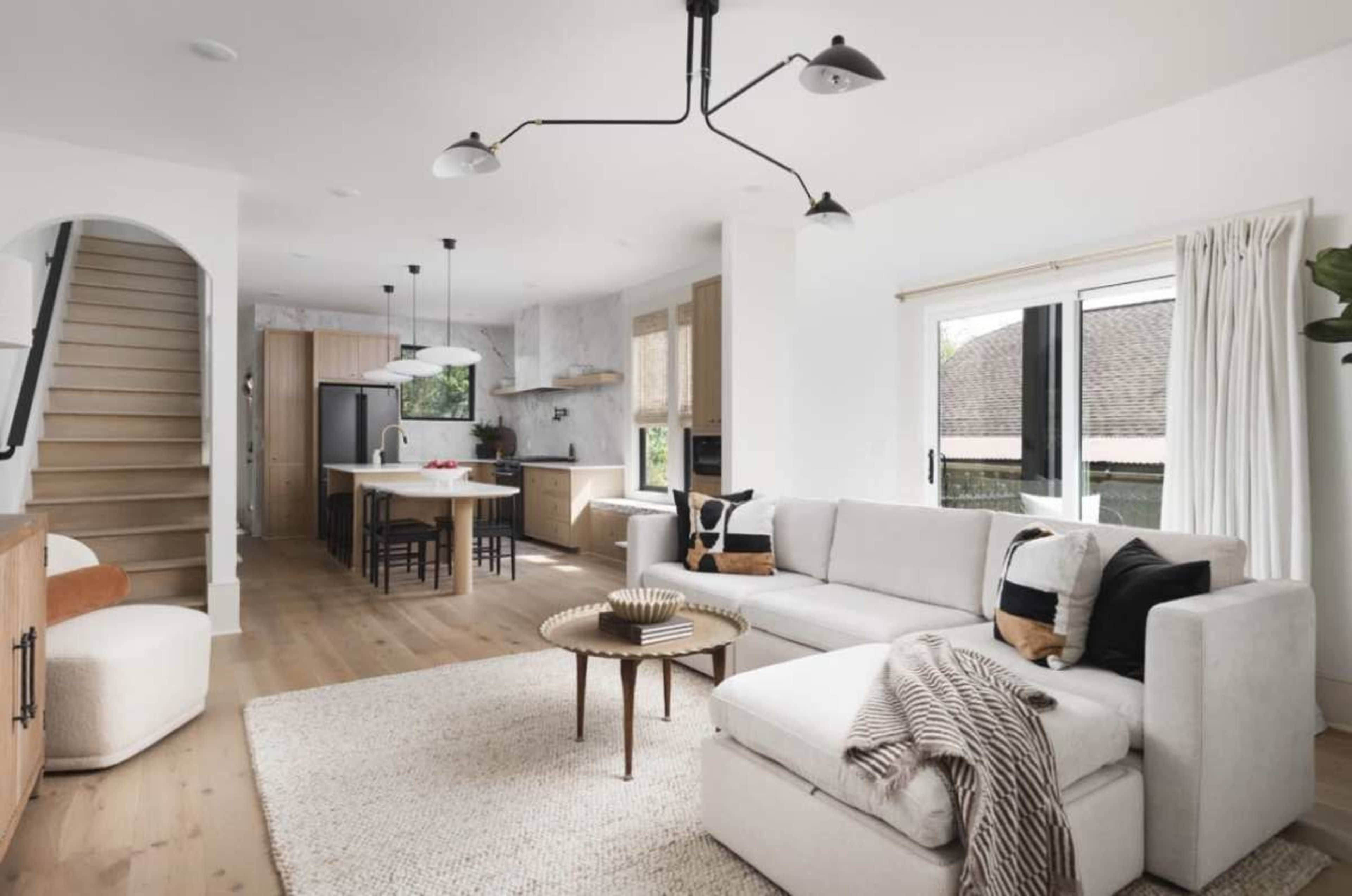 The image features a modern living room with a sectional sofa, a coffee table, and an open-concept kitchen and dining area visible in the background.