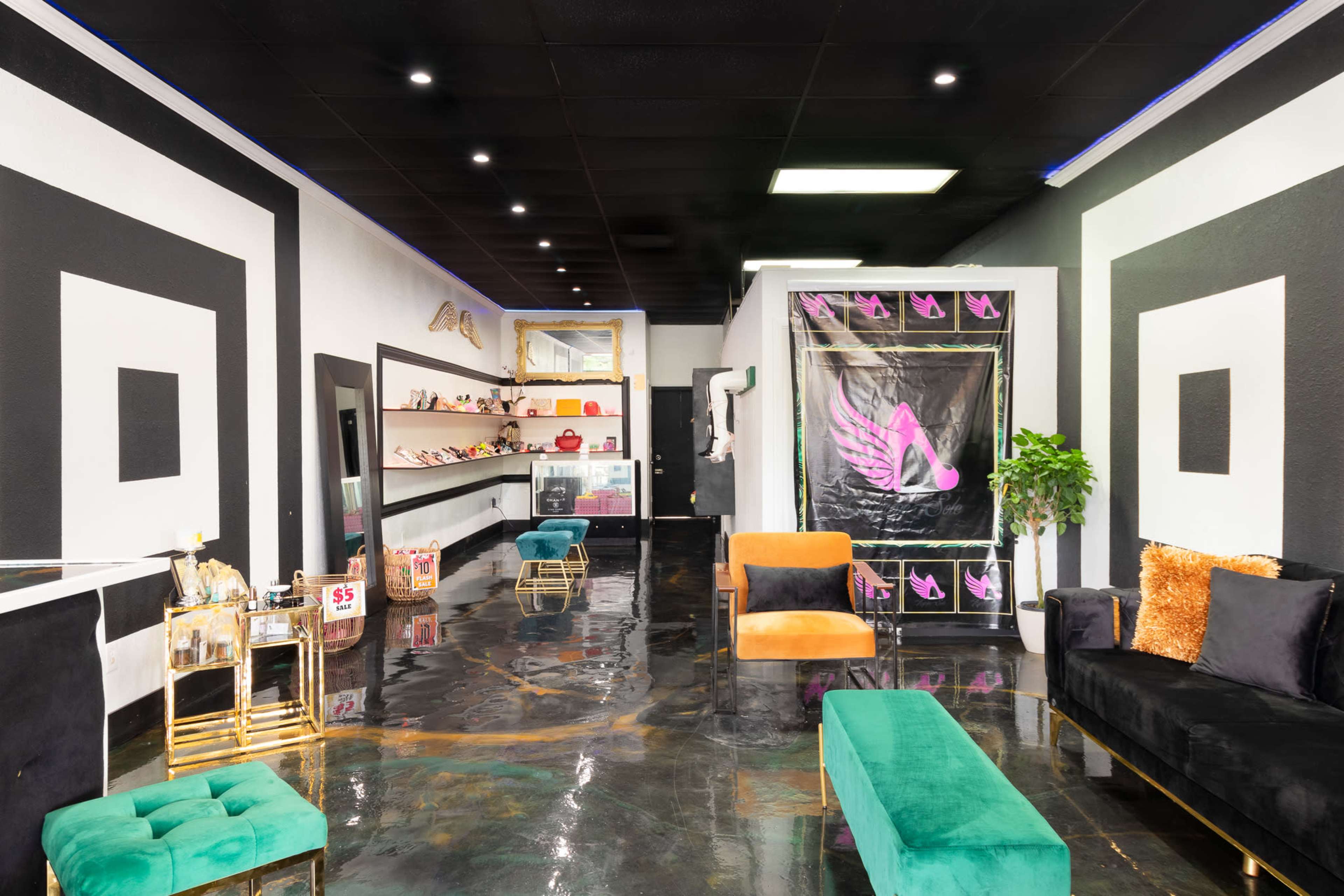 The image shows a modern interior of a boutique with a glossy black floor, black and white geometric wall designs, and seating areas featuring green and black chairs.