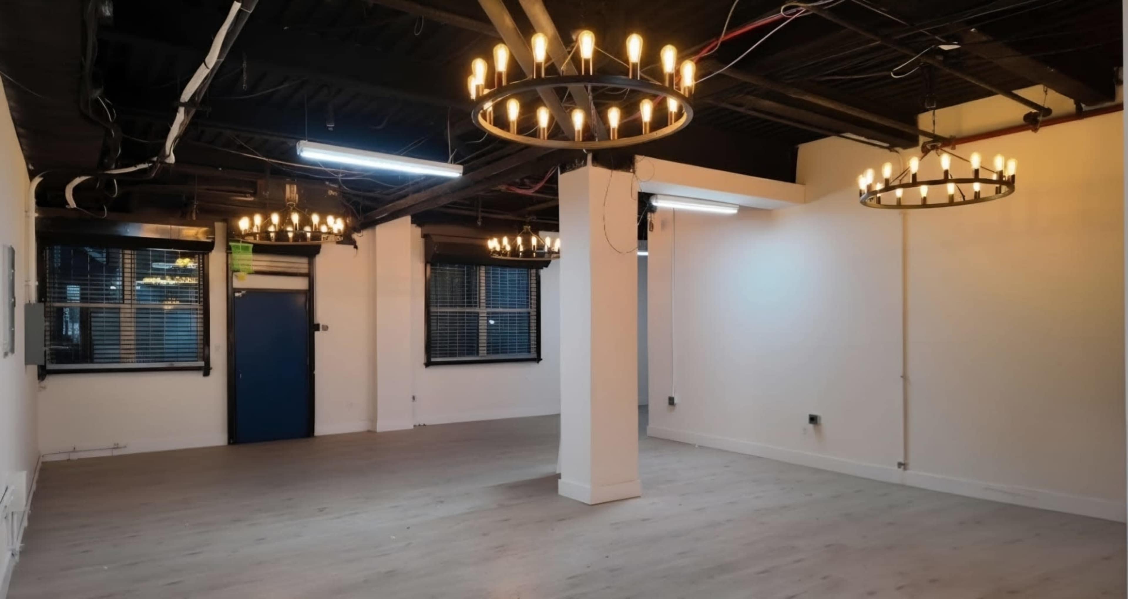 The image depicts a spacious, empty room with wooden flooring and several circular chandeliers hanging from the ceiling.