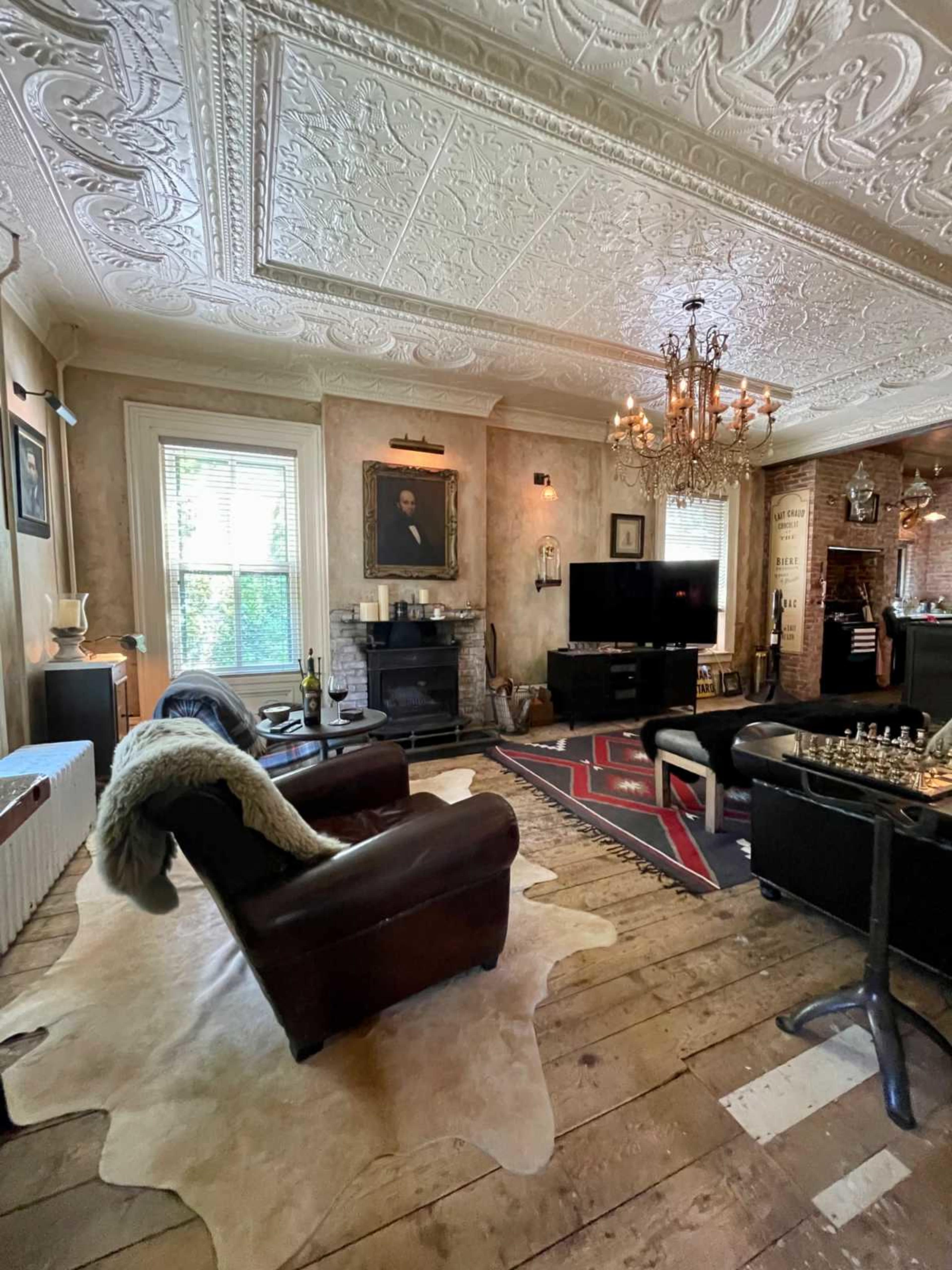 The room features a blend of classic and modern decor, with leather furniture, an ornate ceiling, and a large television.