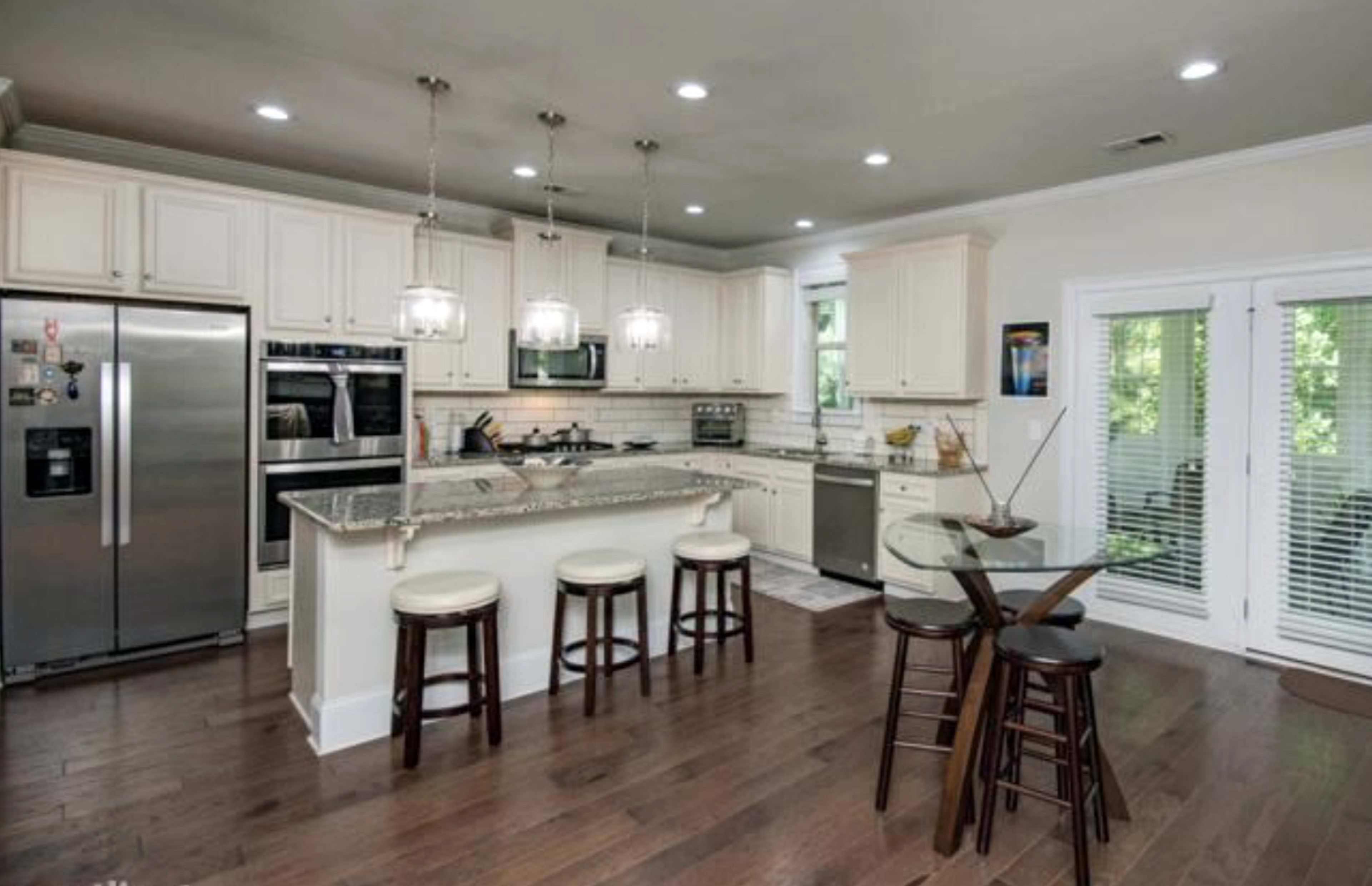 A modern kitchen with white cabinetry, stainless steel appliances, a granite countertop, and a small dining table with four high-backed stools.