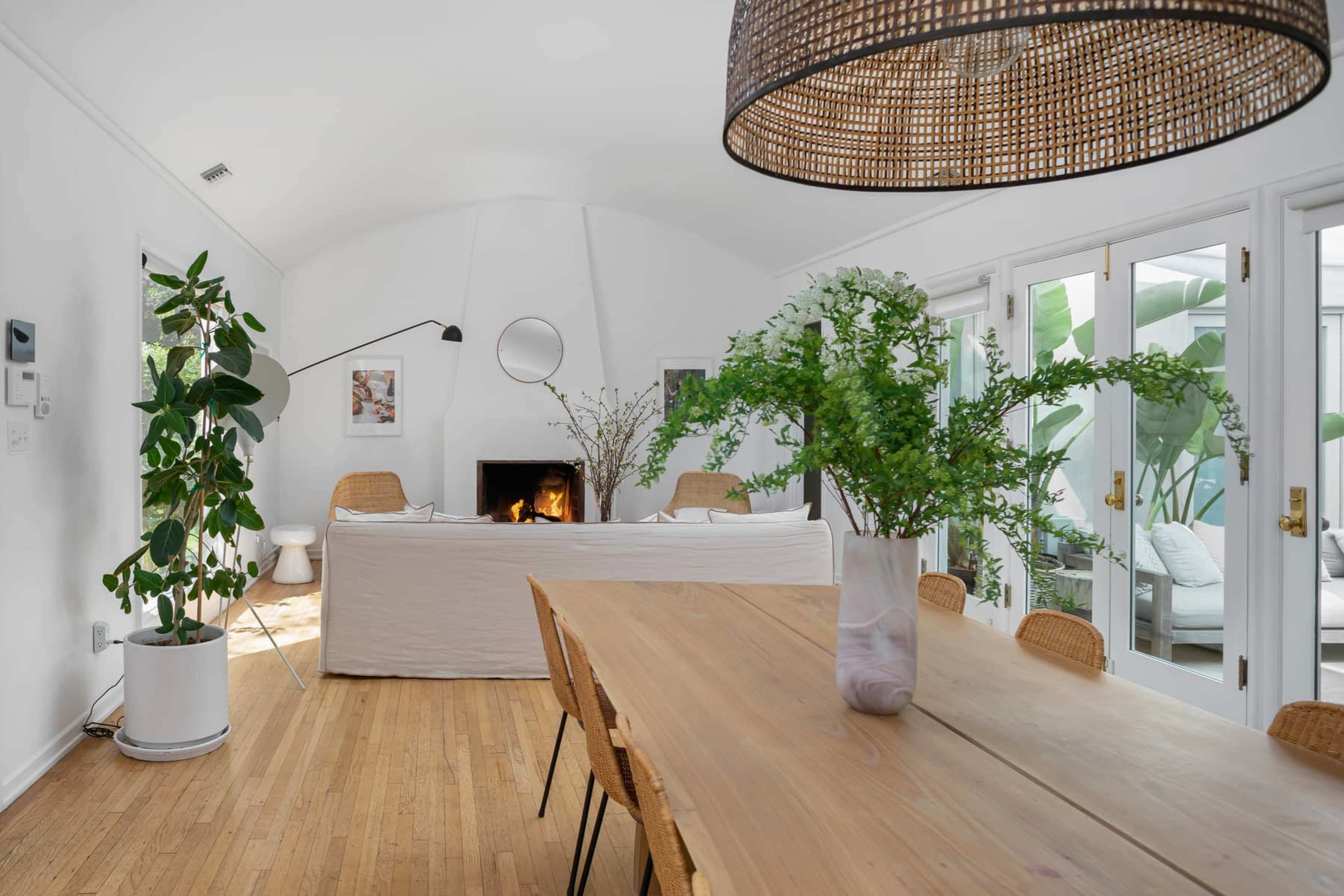 A spacious dining area features a wooden table surrounded by chairs, with a view of a living space that includes a fireplace and large windows.