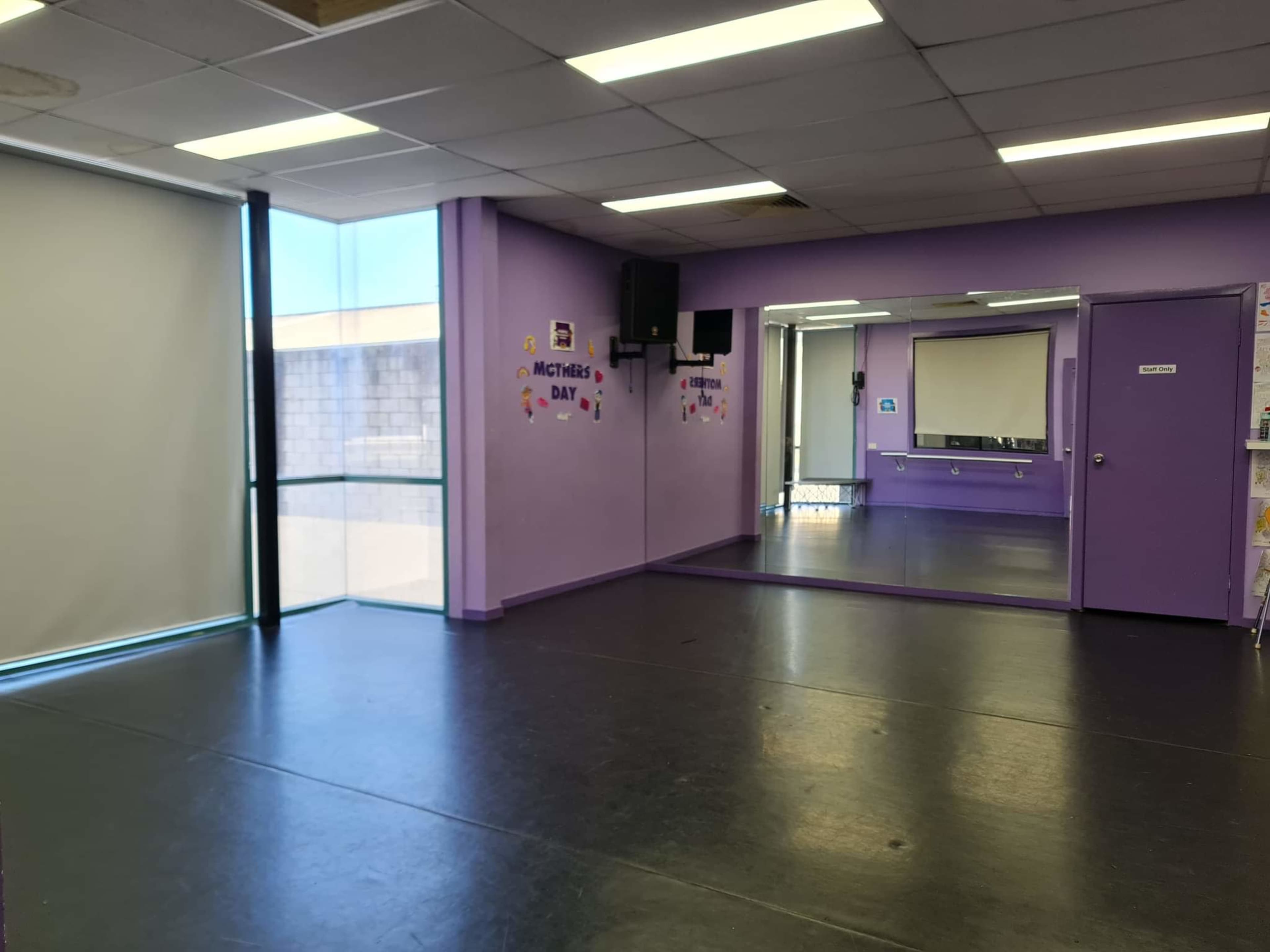 The interior of a purple-walled studio features a large mirror on one side and a window letting in natural light.