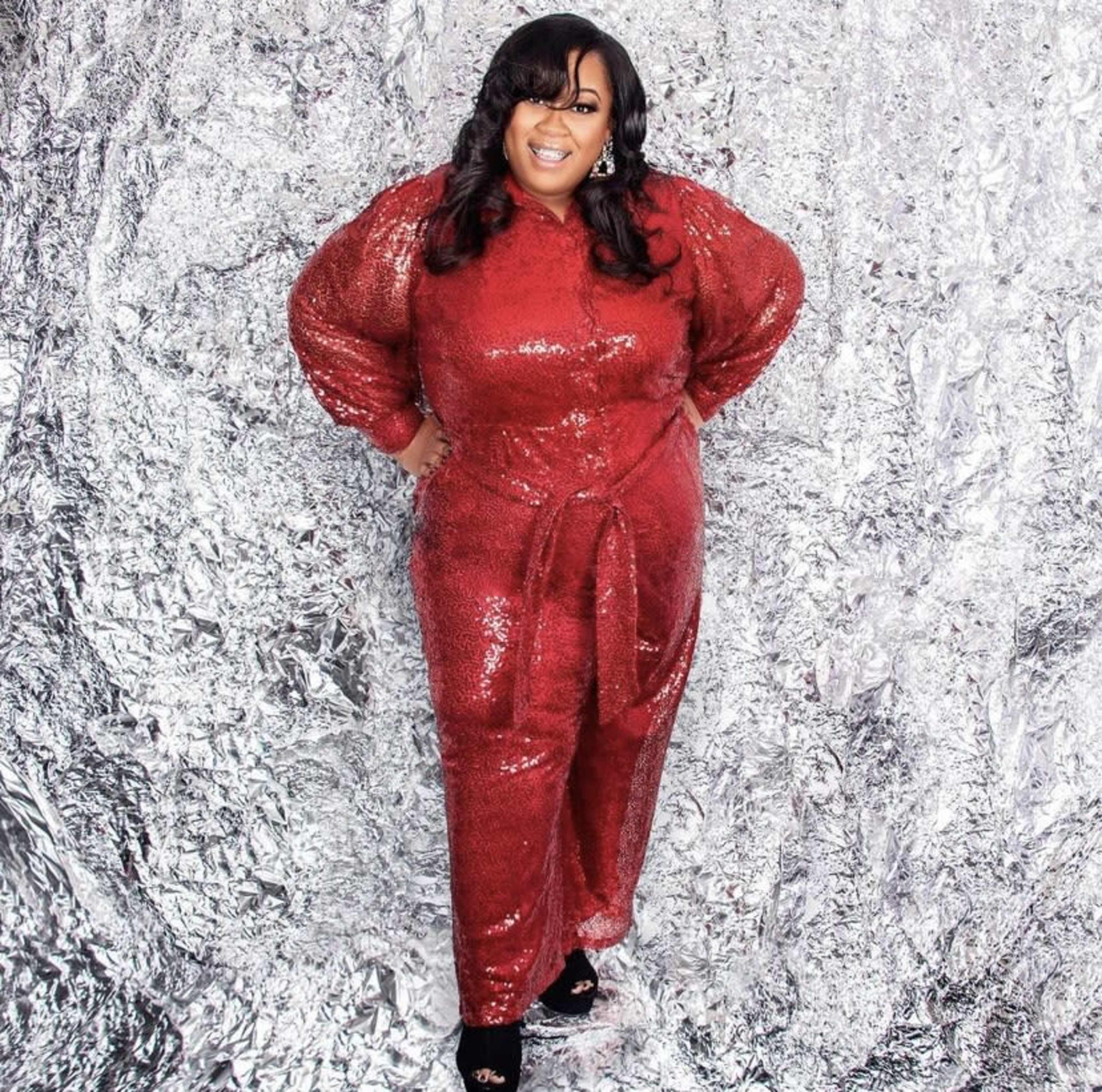 A woman stands confidently in a shiny red sequined outfit against a metallic silver background.