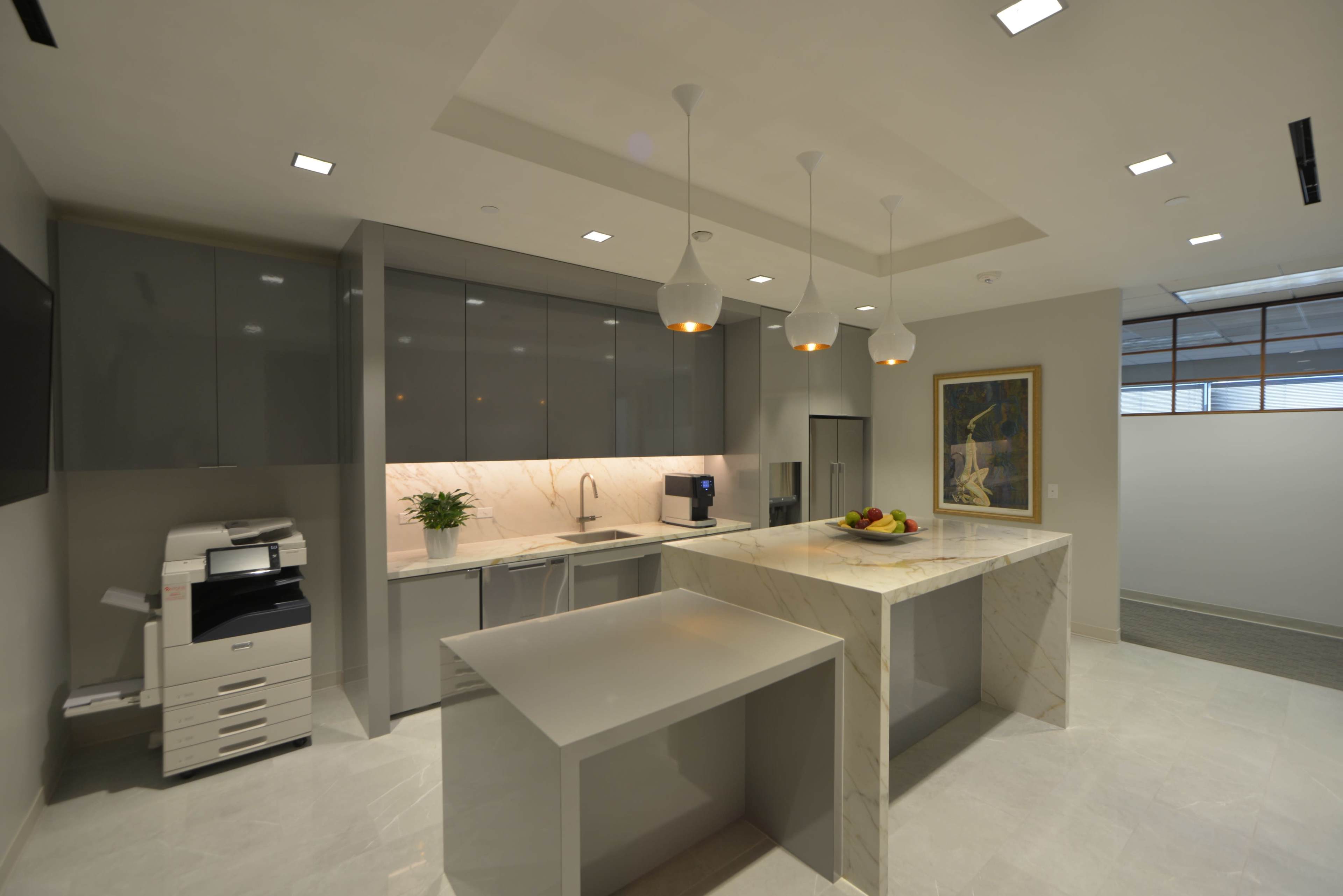 A modern office kitchen with sleek gray cabinetry, a marble island, and pendant lighting.