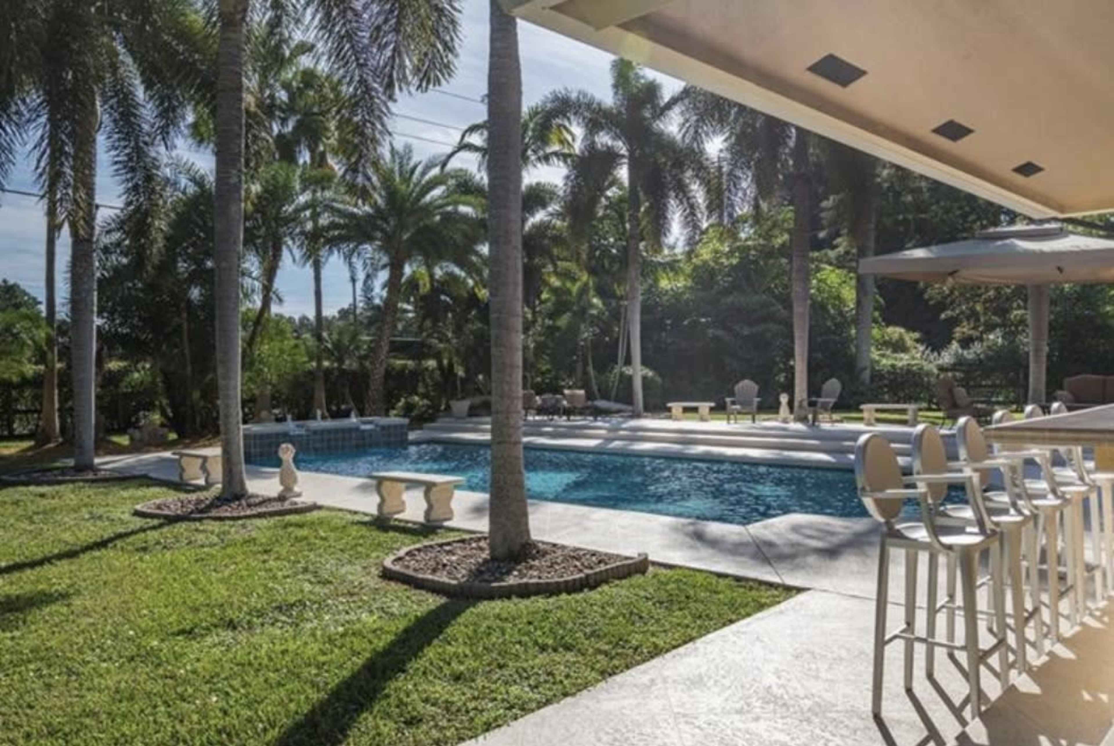 A swimming pool surrounded by palm trees and grass is visible from a patio with seating.