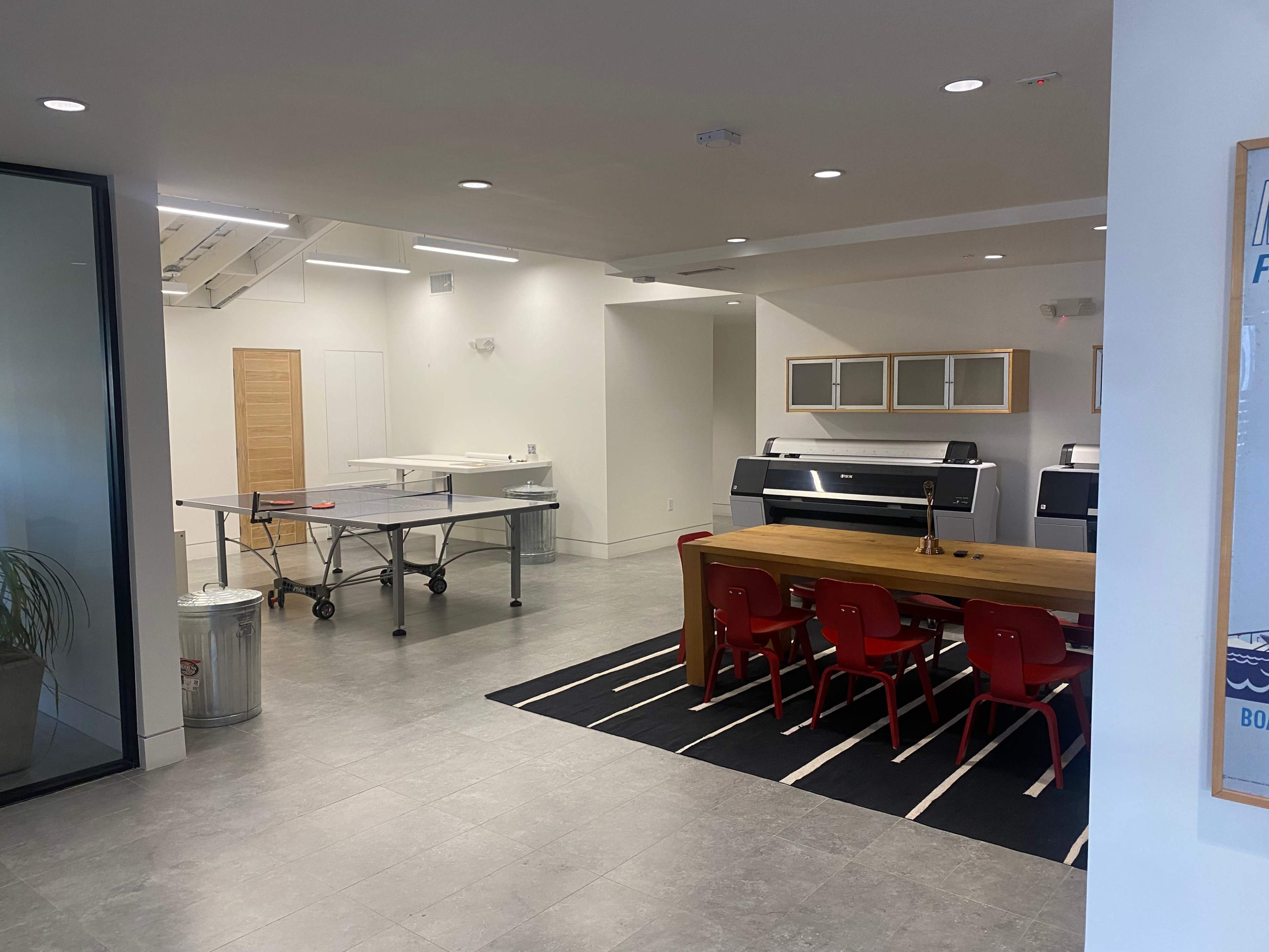 A modern office space featuring a dining table with red chairs, a ping pong table, and a sleek design aesthetic.