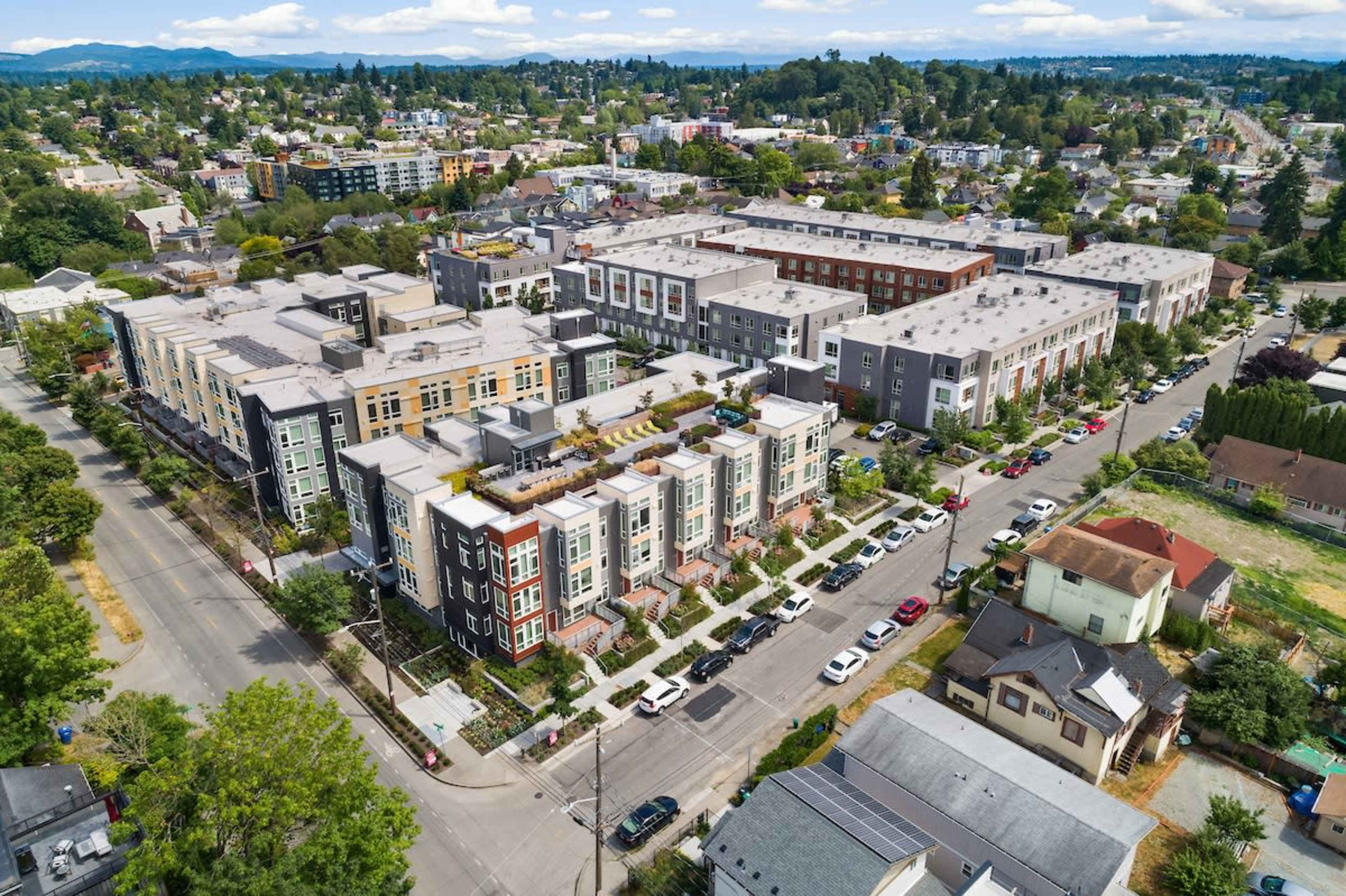 An aerial view captures a residential neighborhood featuring several multi-story apartment buildings and a tree-lined street alongside parked cars.