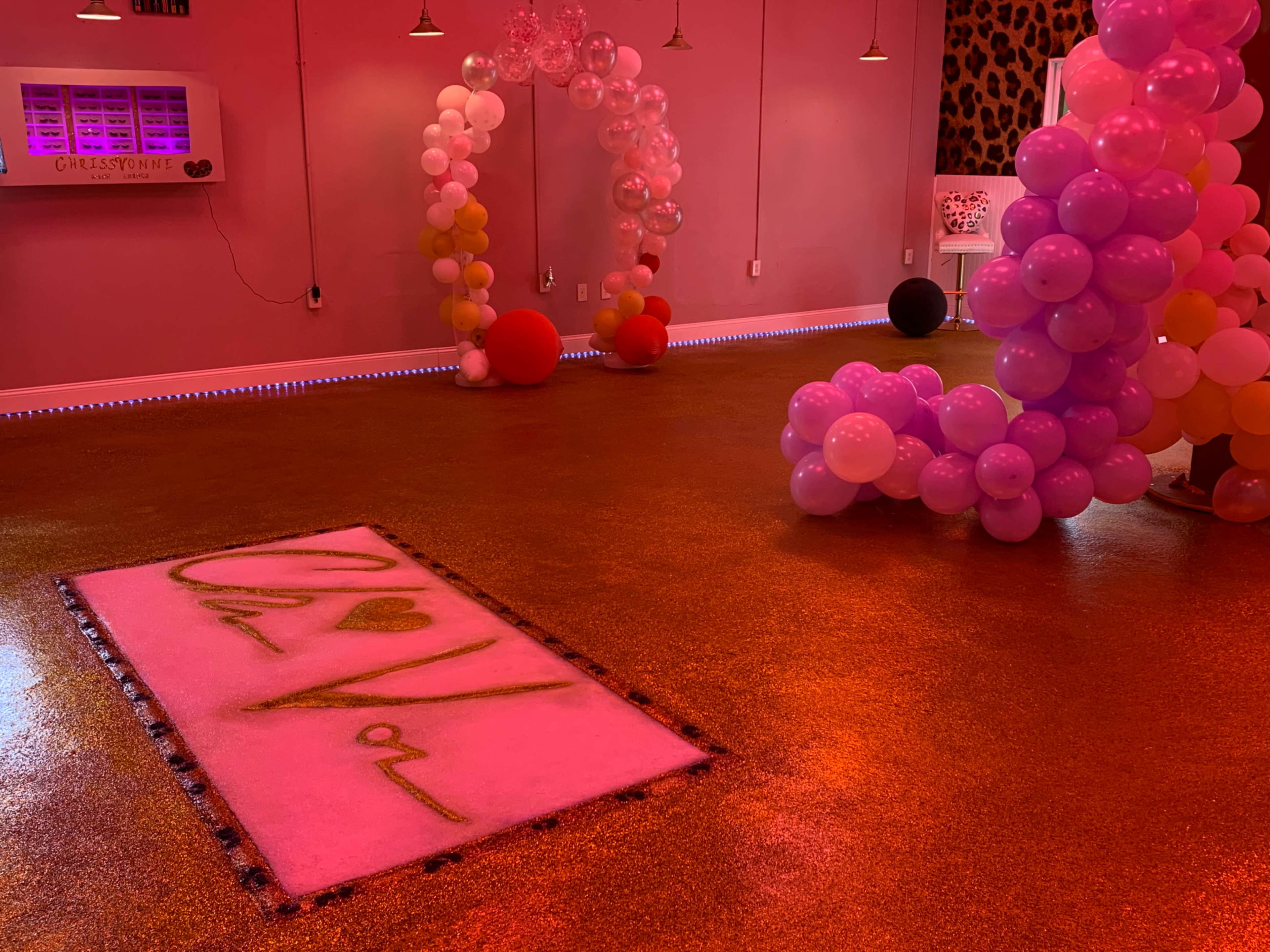 The scene features a brightly colored event space with pink walls, balloon arches, and a decorative floor mat that reads "Chavon."