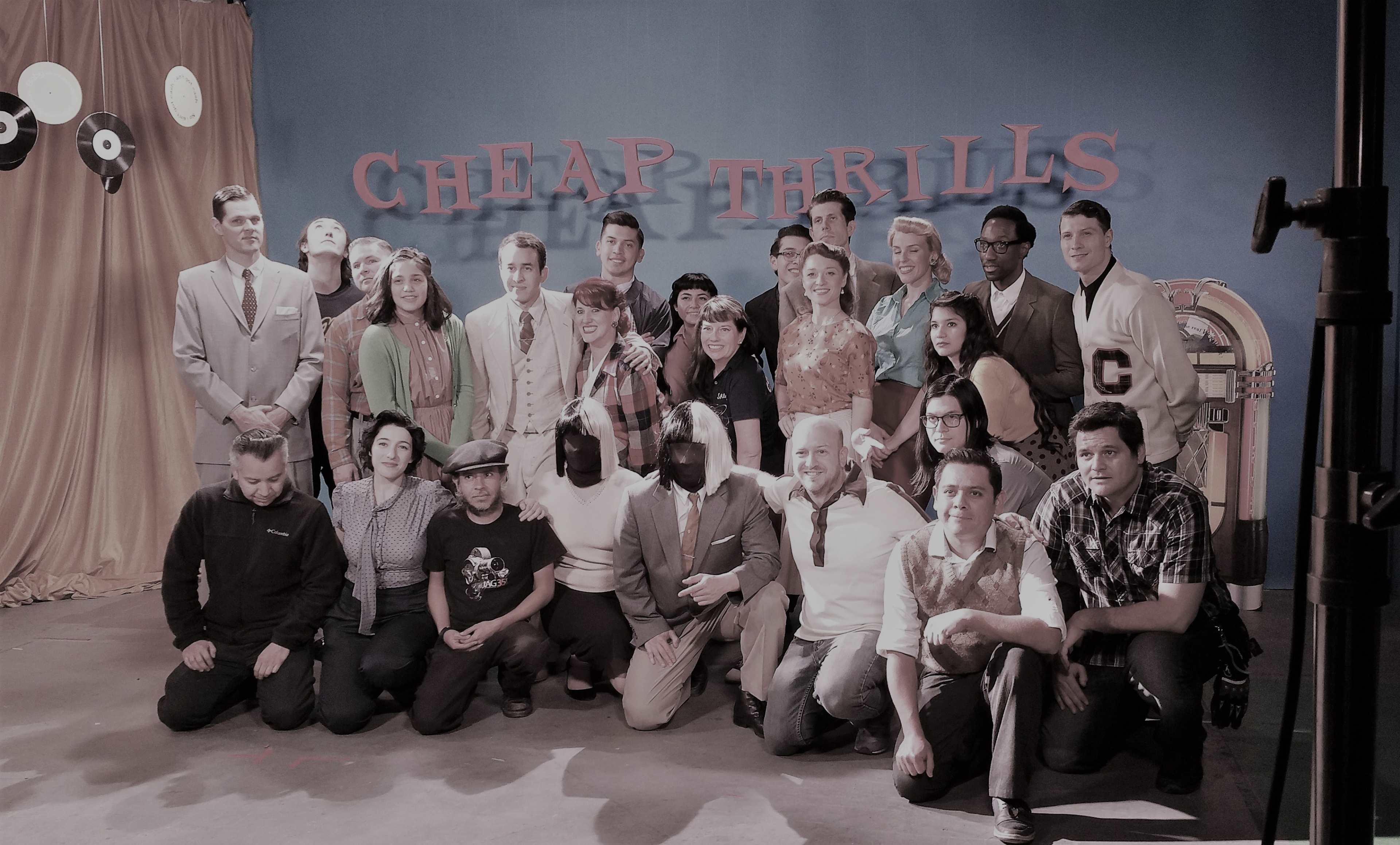 A group of approximately thirty people poses together in a room decorated with a vintage jukebox and a backdrop reading "CHEAP THRILLS."