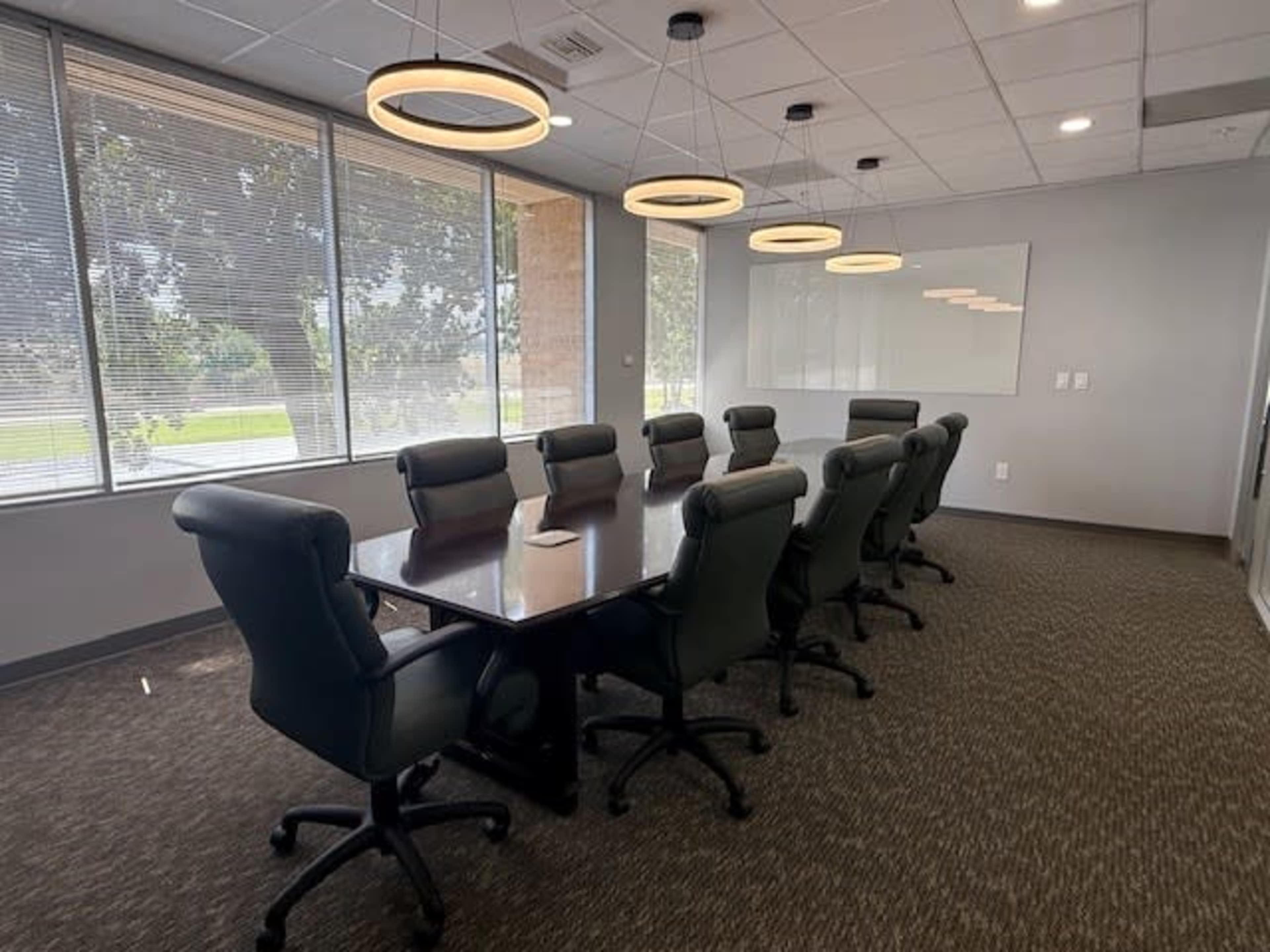 The image shows a conference room with a long table surrounded by eight office chairs, and pendant lighting hanging from the ceiling.
