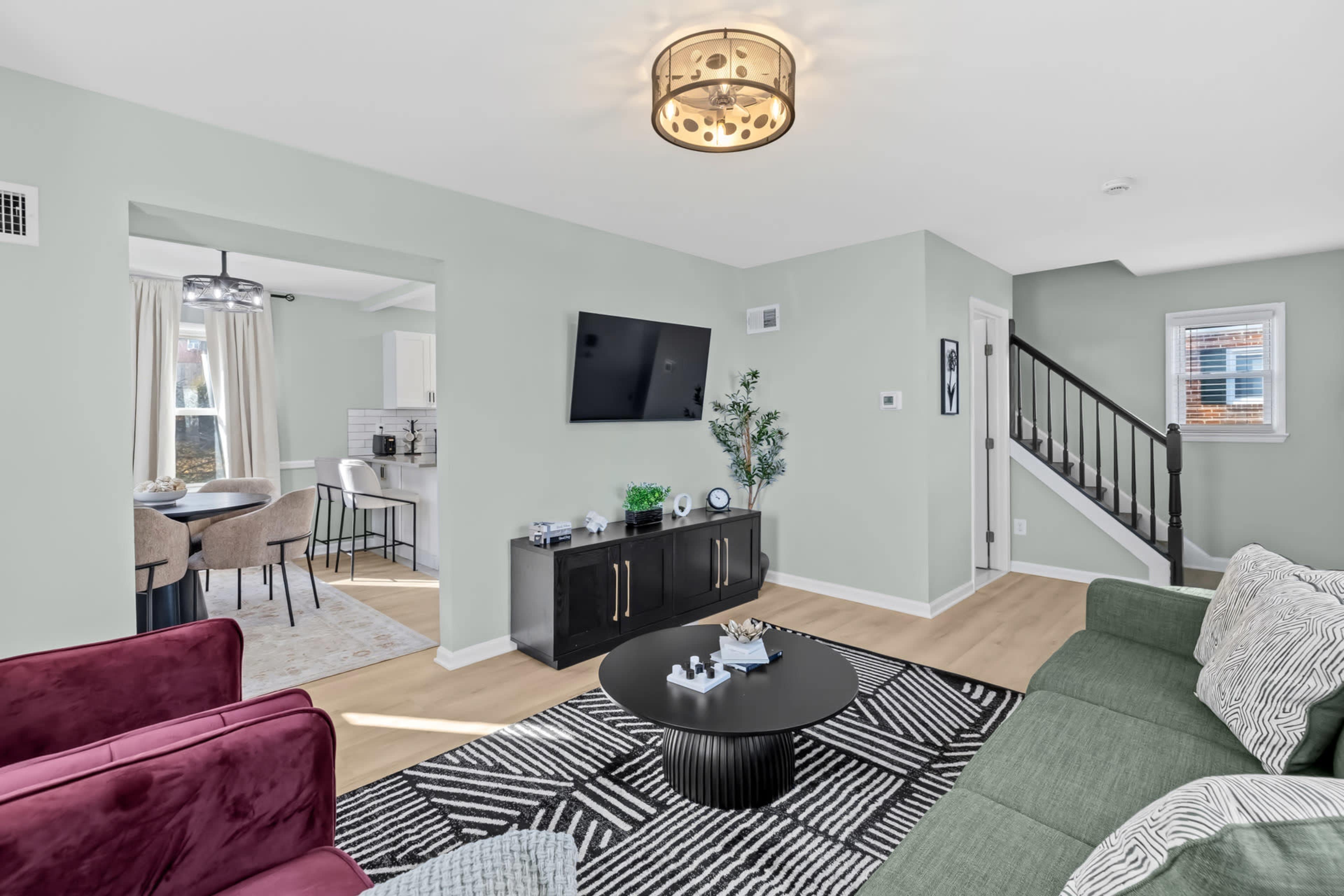 The image shows a modern living room with a green sofa, a black coffee table, and a mounted television, featuring light green walls and hardwood flooring.