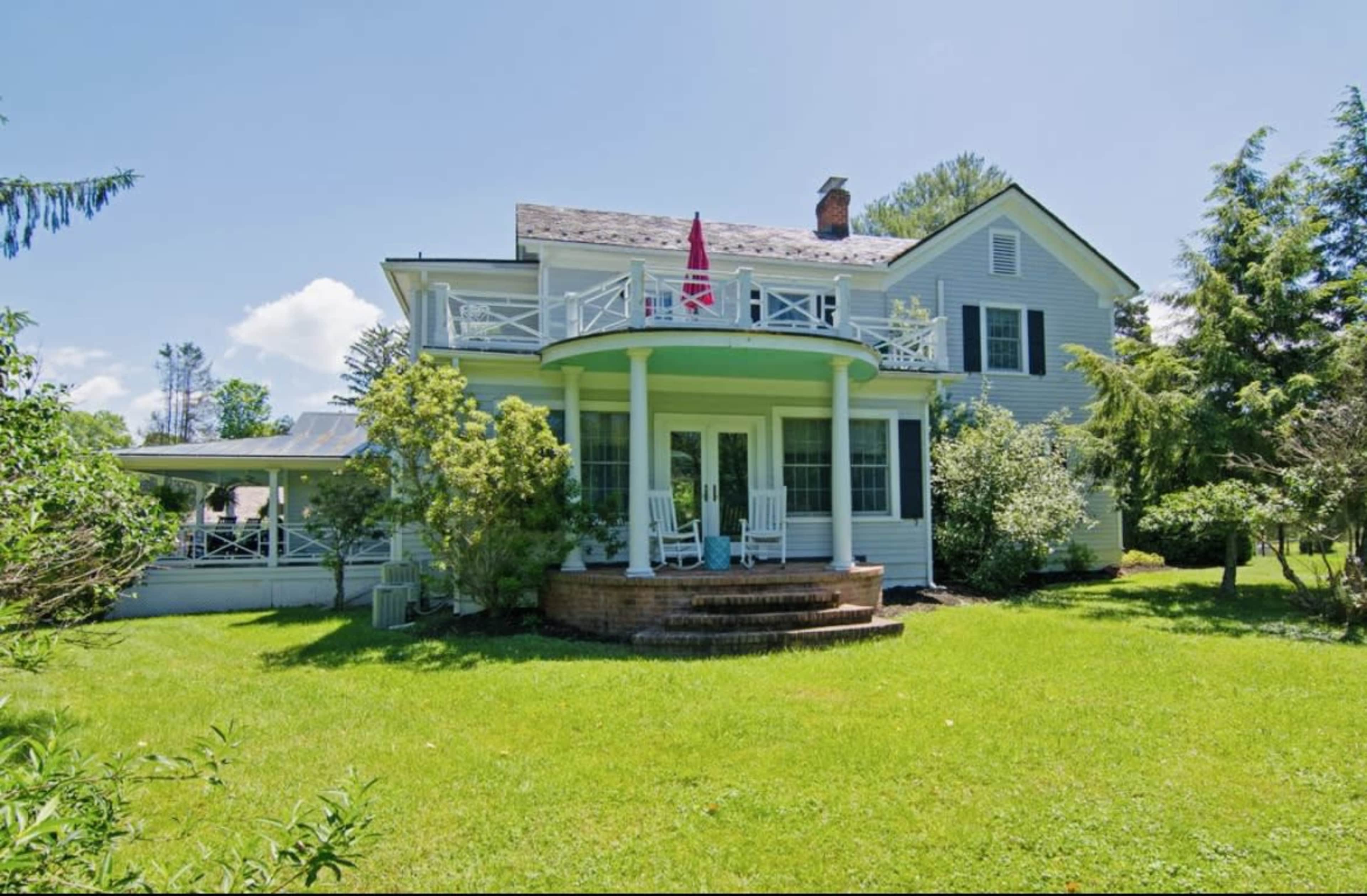 A large, two-story house with a curved porch, surrounded by green lawn and trees.