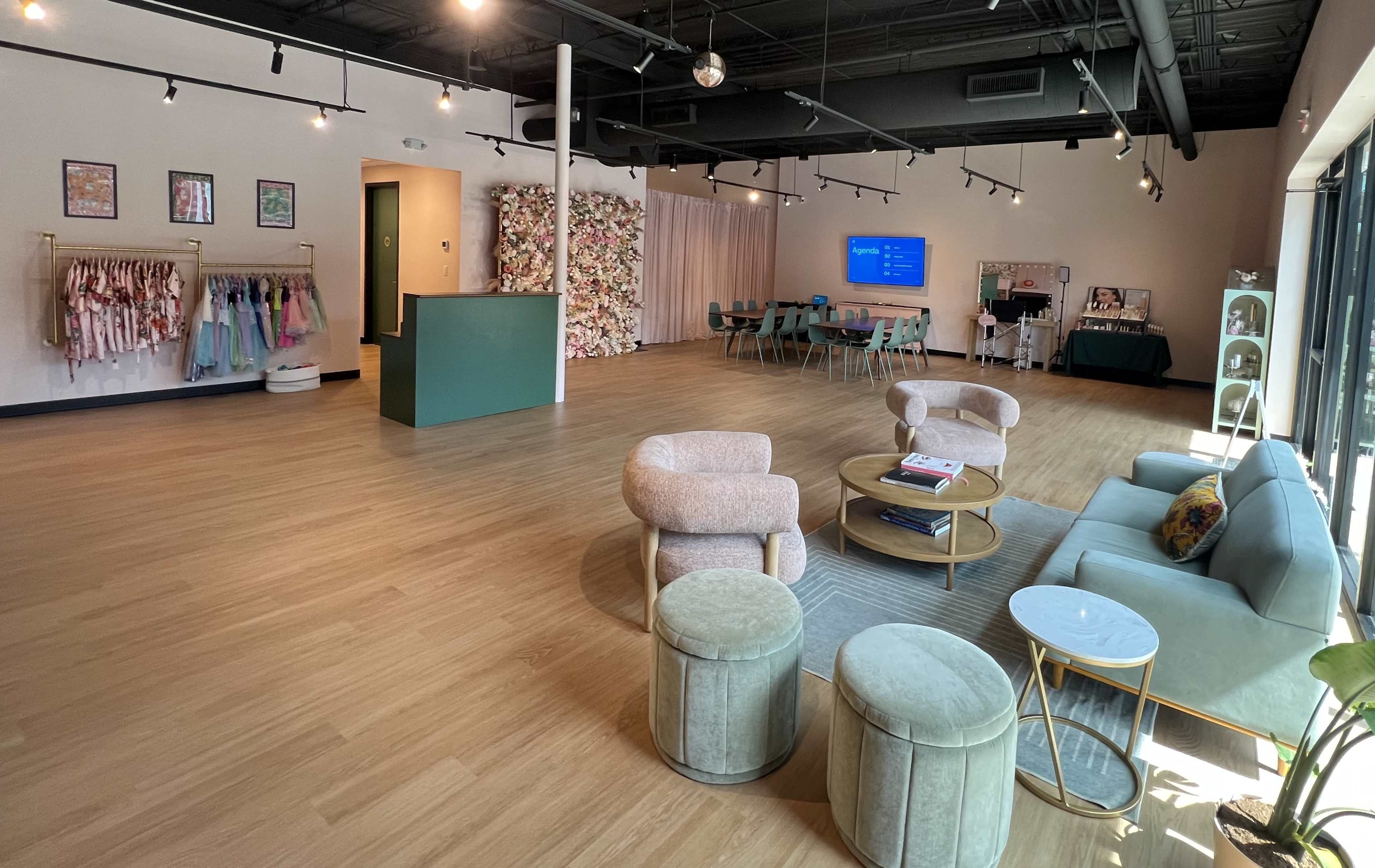 The image shows a spacious, well-lit interior that features a seating area with soft seating, a reception desk, and a rack displaying colorful clothing along one wall.