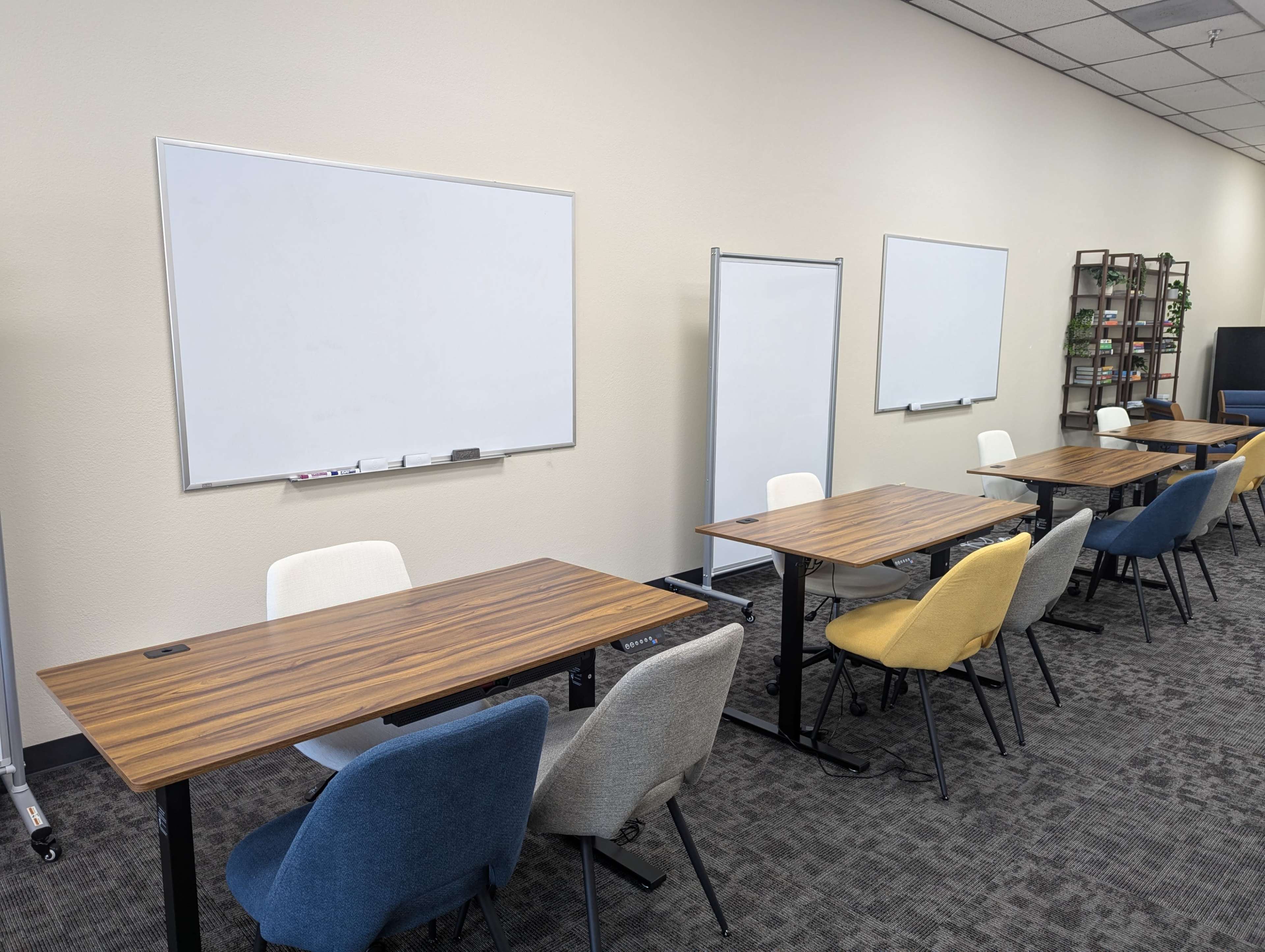 A modern classroom or meeting room with several tables and chairs arranged around whiteboards on a beige wall.