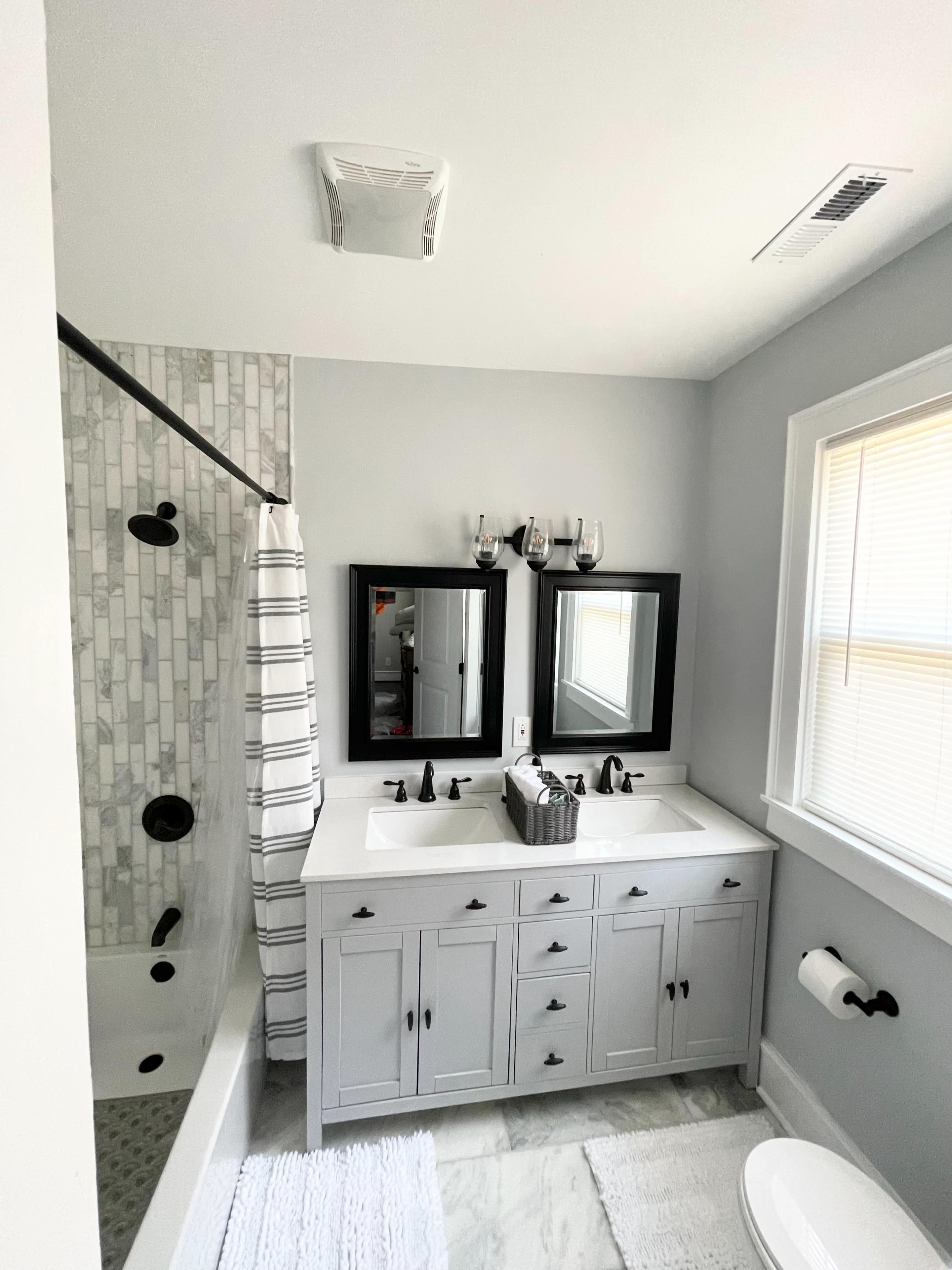 A modern bathroom featuring a dual sink vanity, a tub with a shower, and a gray color scheme.