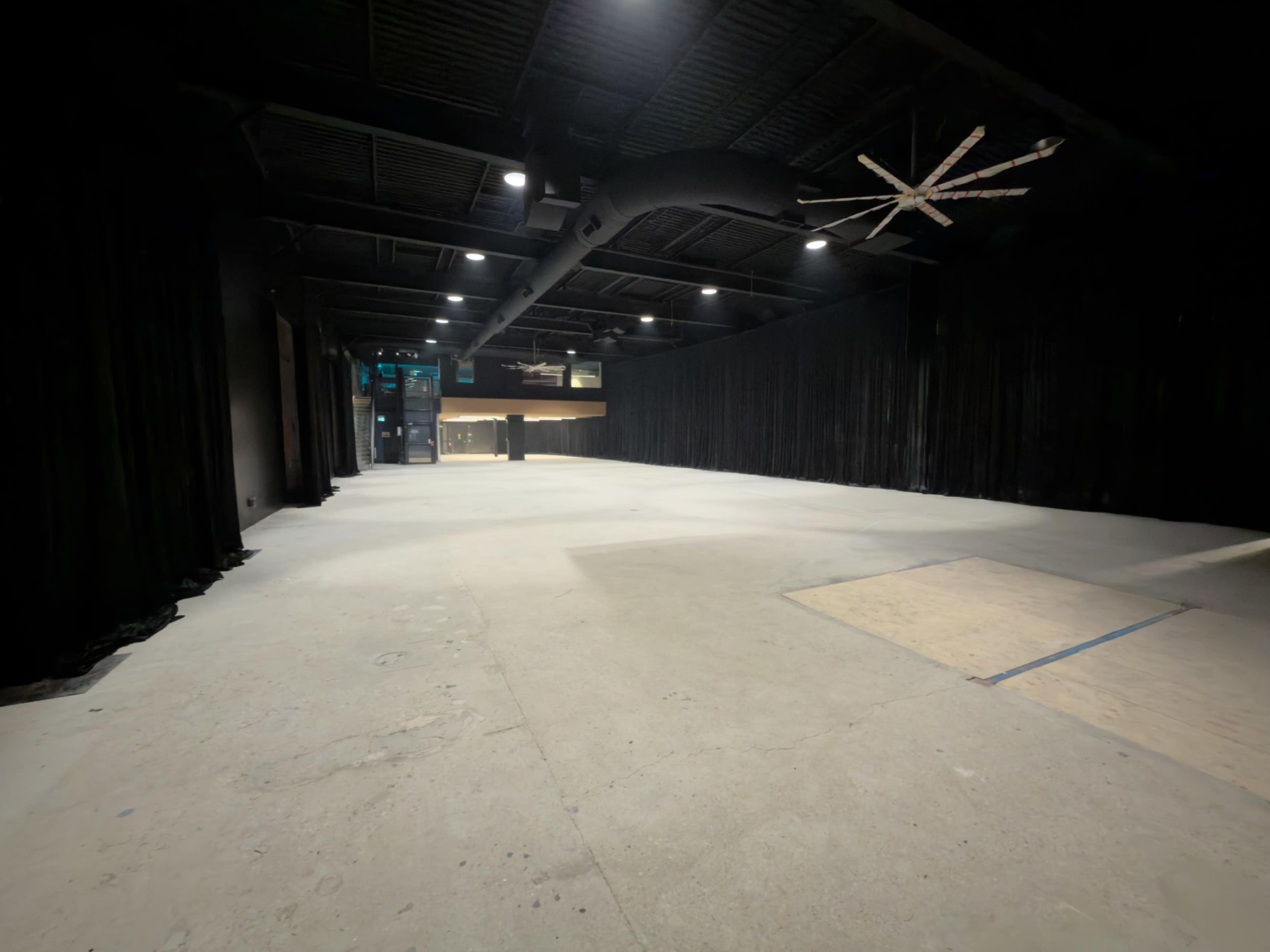 The image shows an empty, dimly lit industrial space with black curtains lining the walls and a concrete floor.