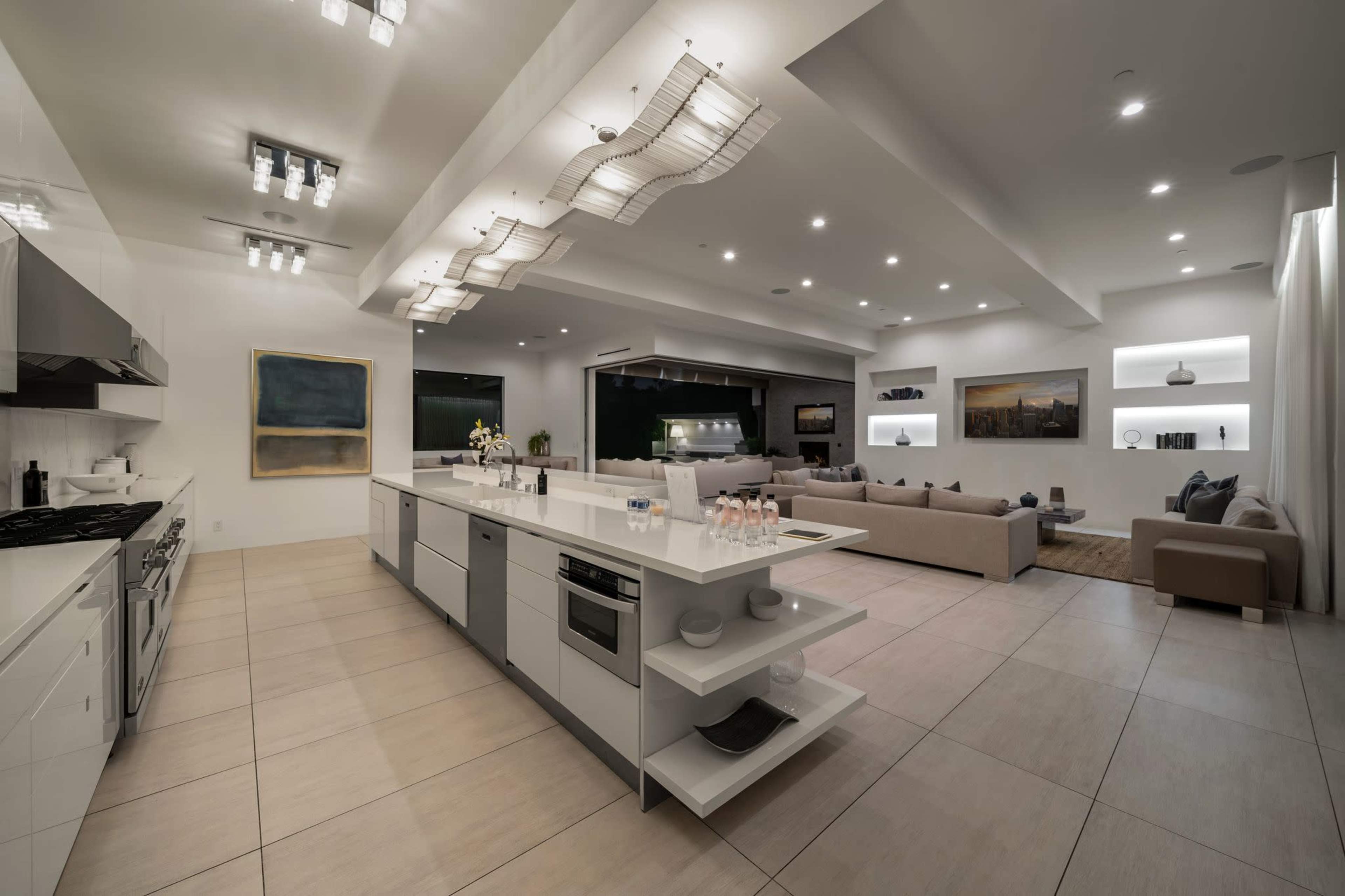 A modern, open-concept kitchen and living area with sleek, white cabinetry, a central island, and a spacious seating arrangement.