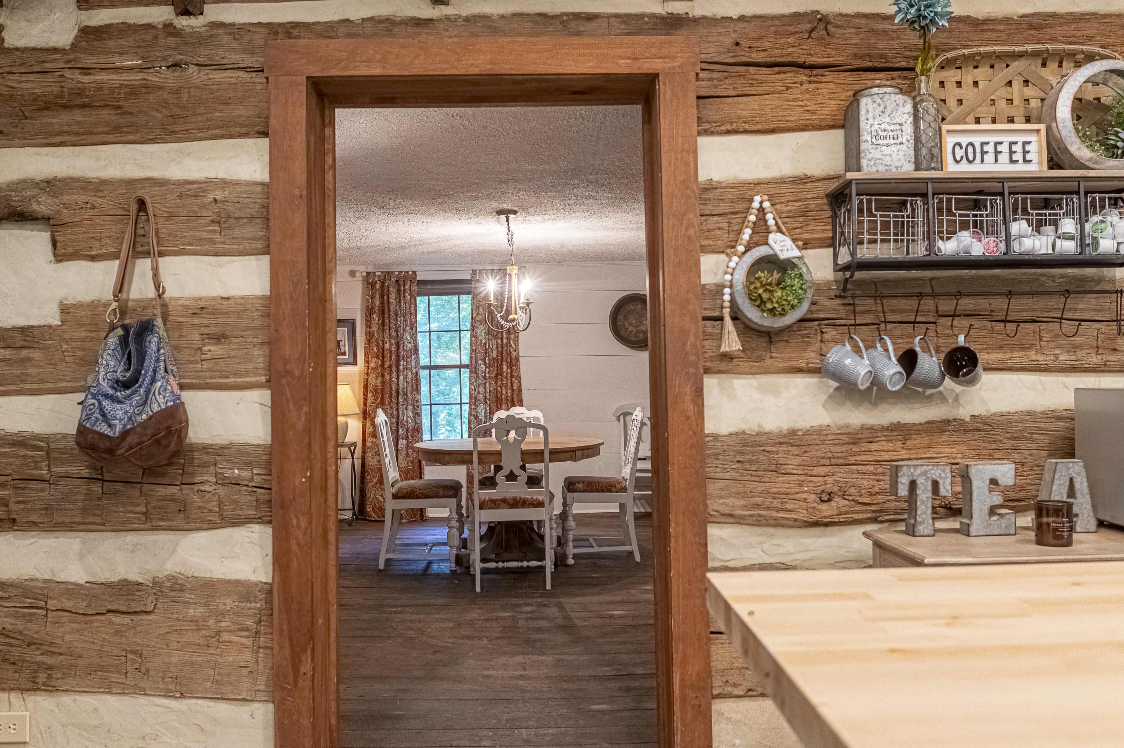 A wooden interior with a doorway leading to a dining area furnished with a round table and chairs, surrounded by rustic decor.
