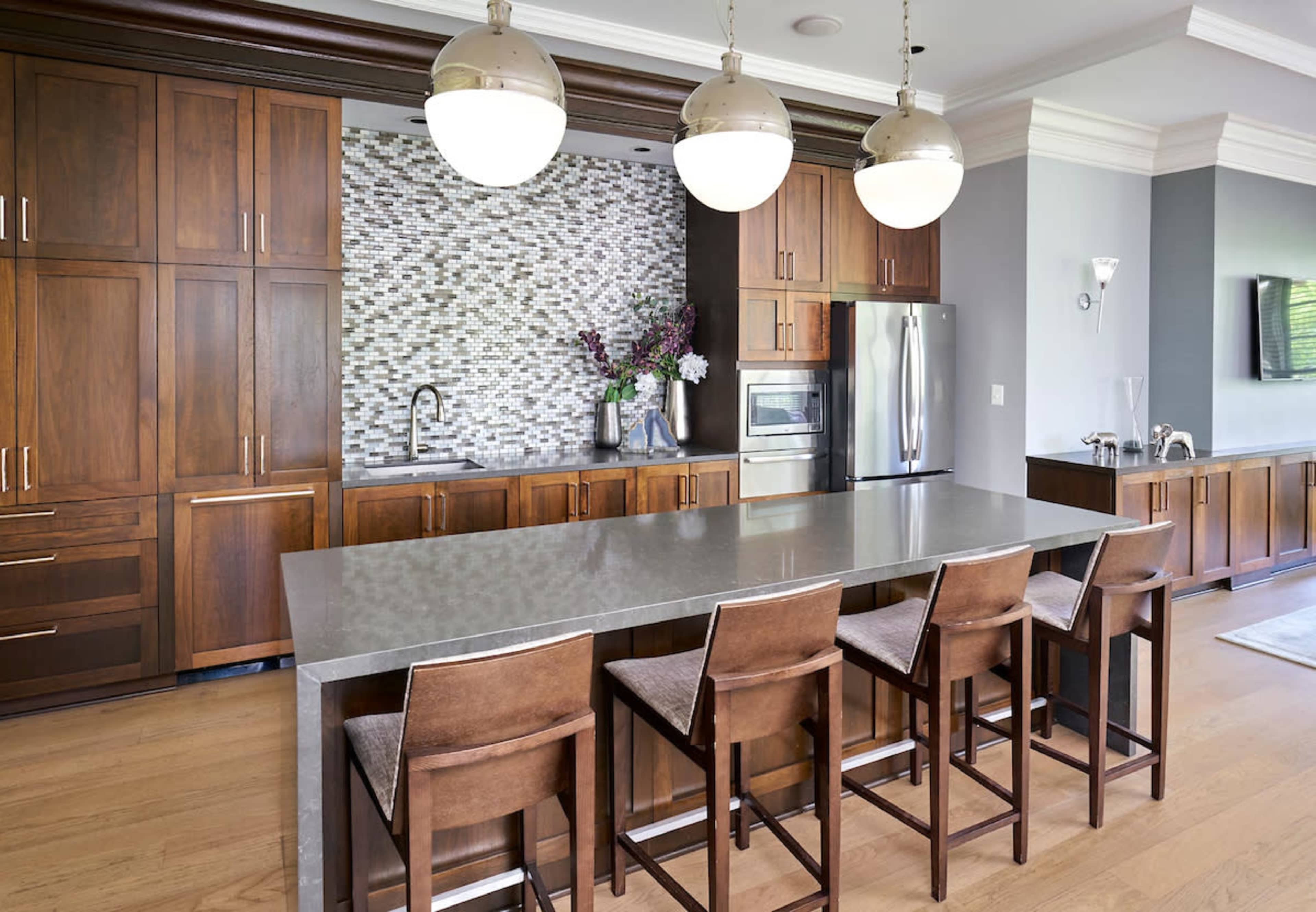 The image shows a modern kitchen with dark wood cabinetry, a large gray stone island, and pendant lighting above it.