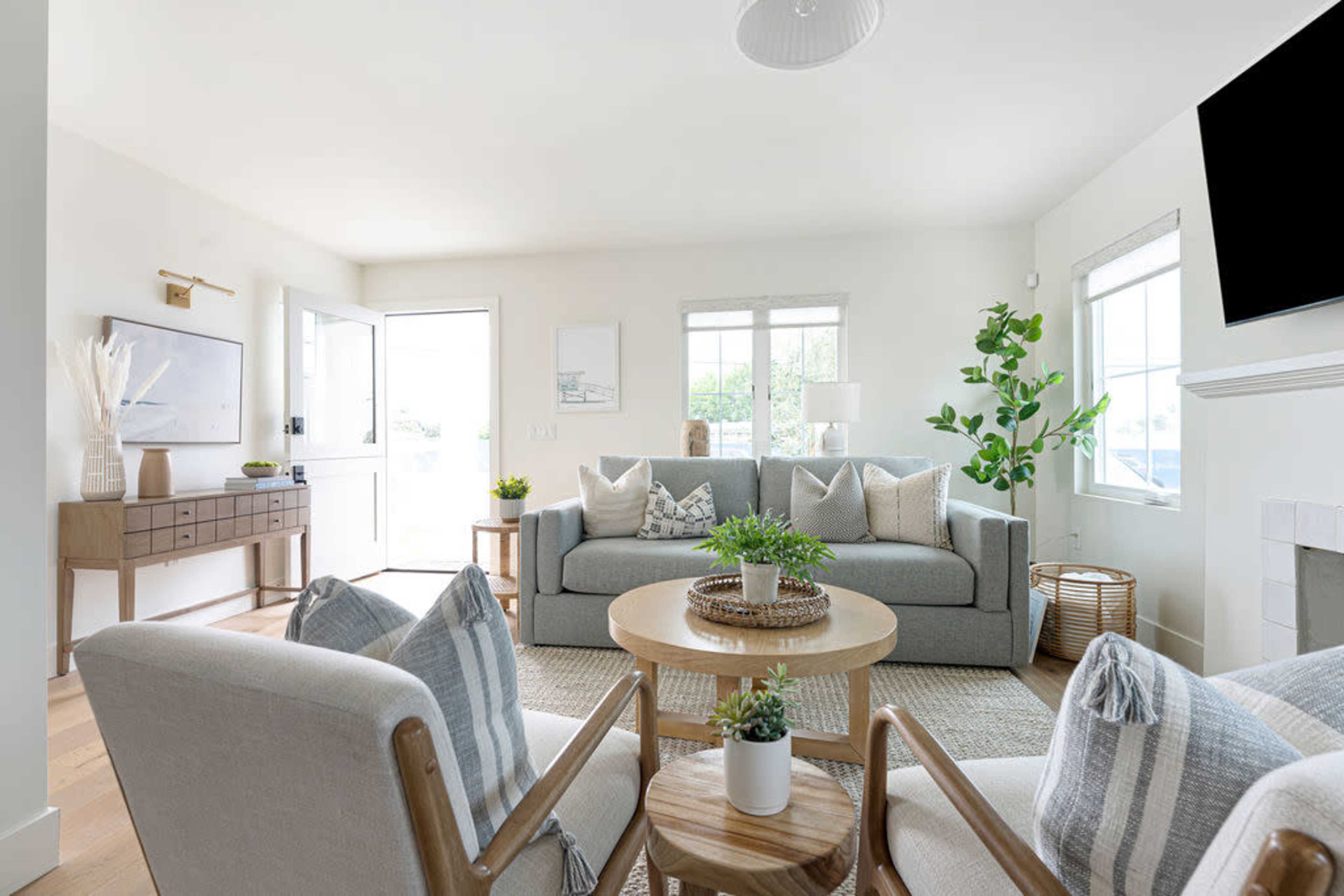 The living room features a light-colored sofa, two armchairs, a round coffee table, and a console table, with large windows allowing natural light to enter.