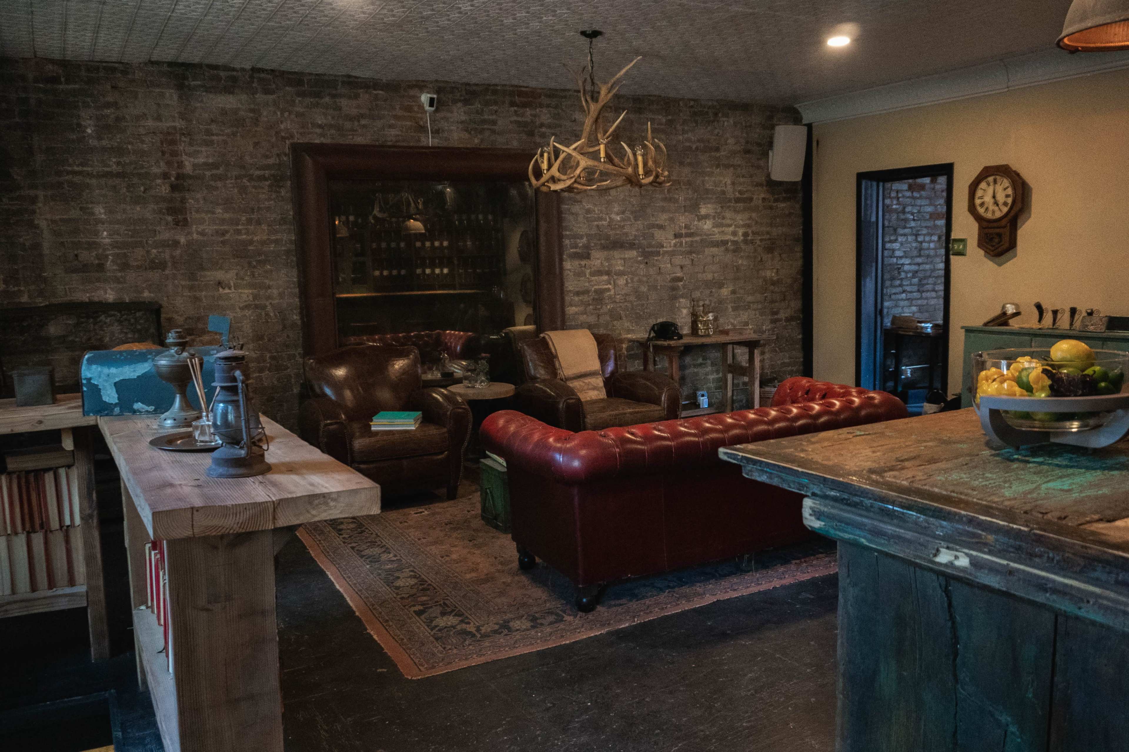 A cozy lounge area with leather armchairs, a tufted red sofa, a wooden table, and exposed brick walls.