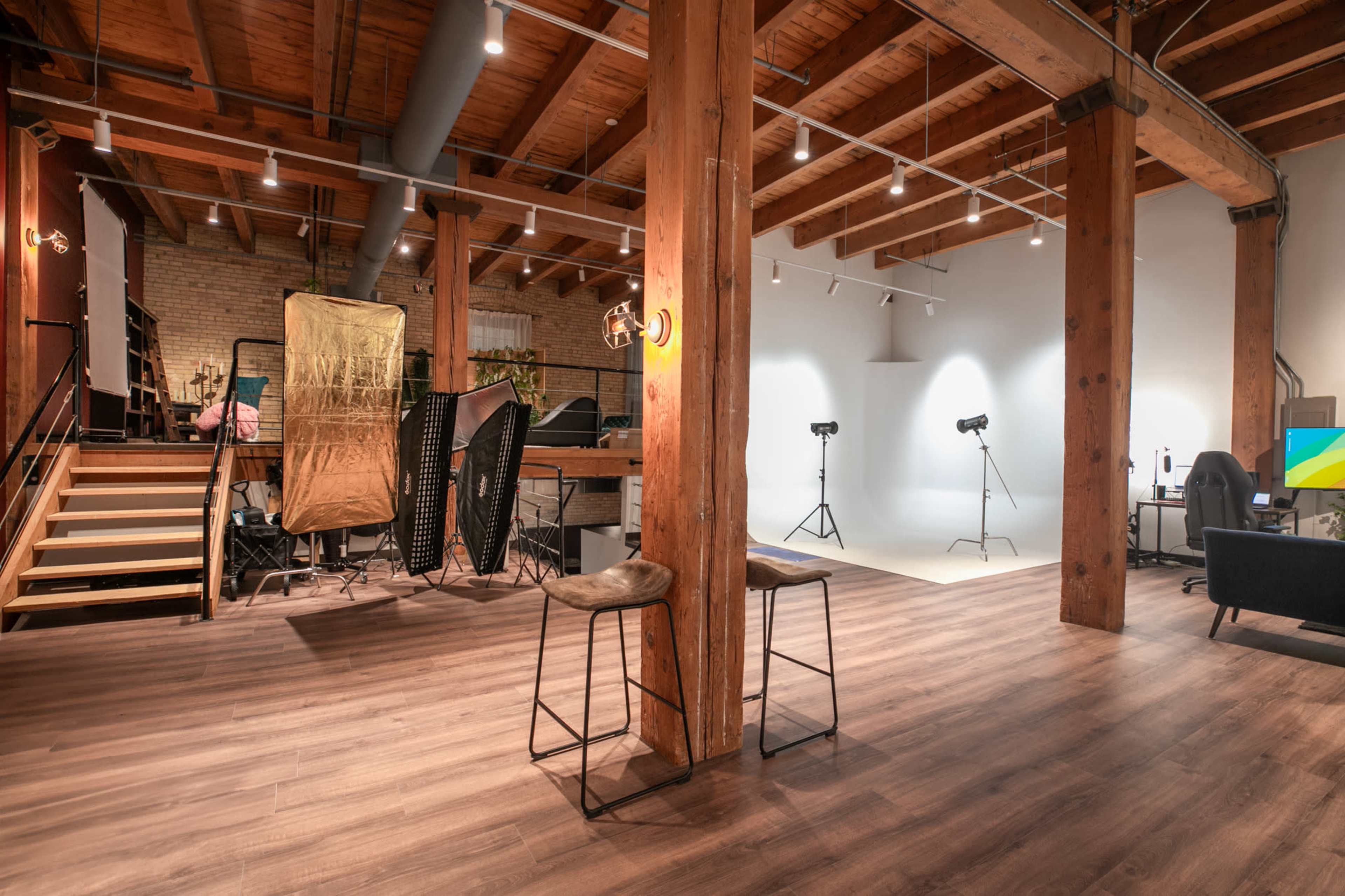 A spacious photography studio features wooden beams, a light-colored backdrop, and various equipment arranged around the area.