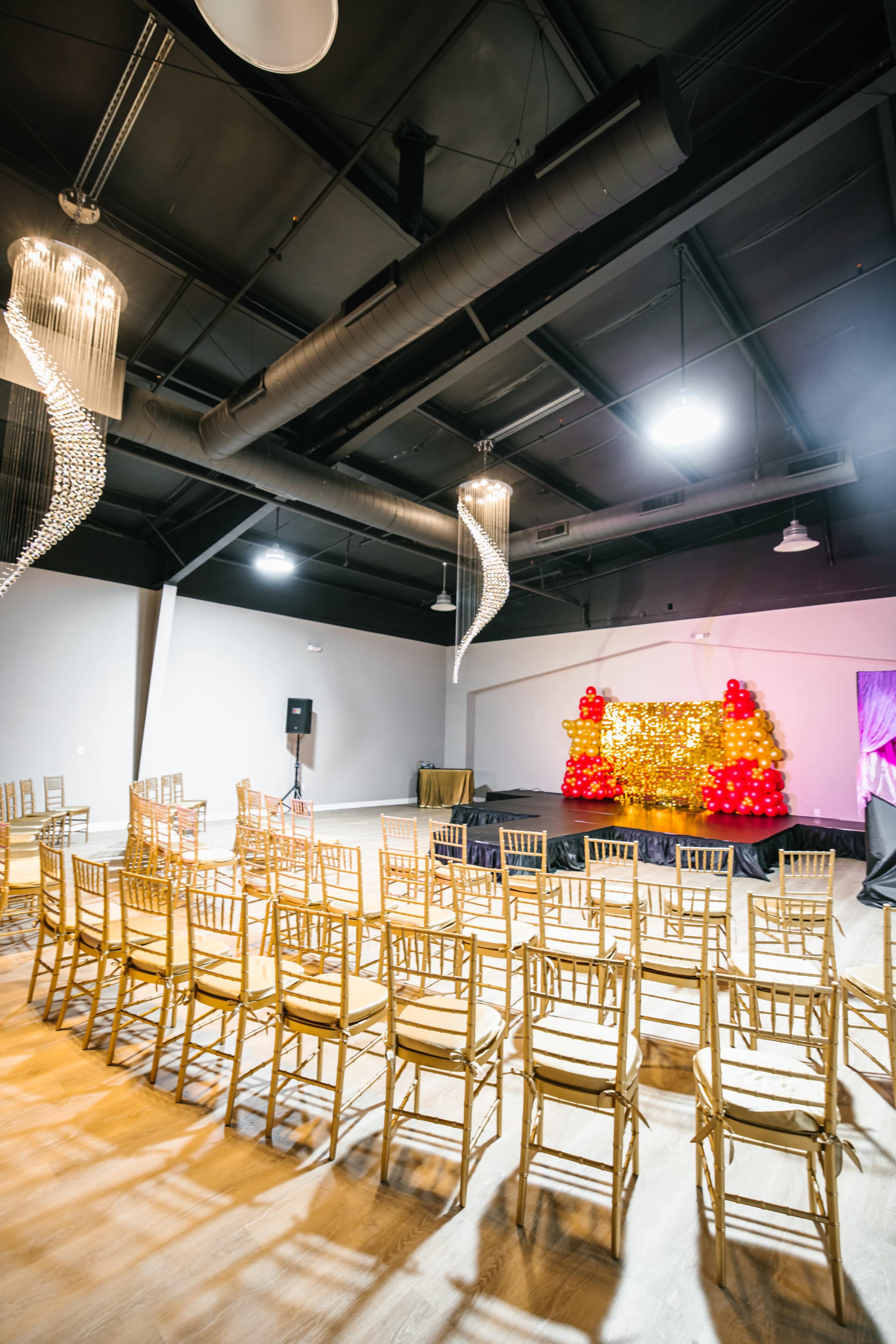 A spacious event venue with rows of gold chairs facing a decorated stage featuring red and gold decorations.