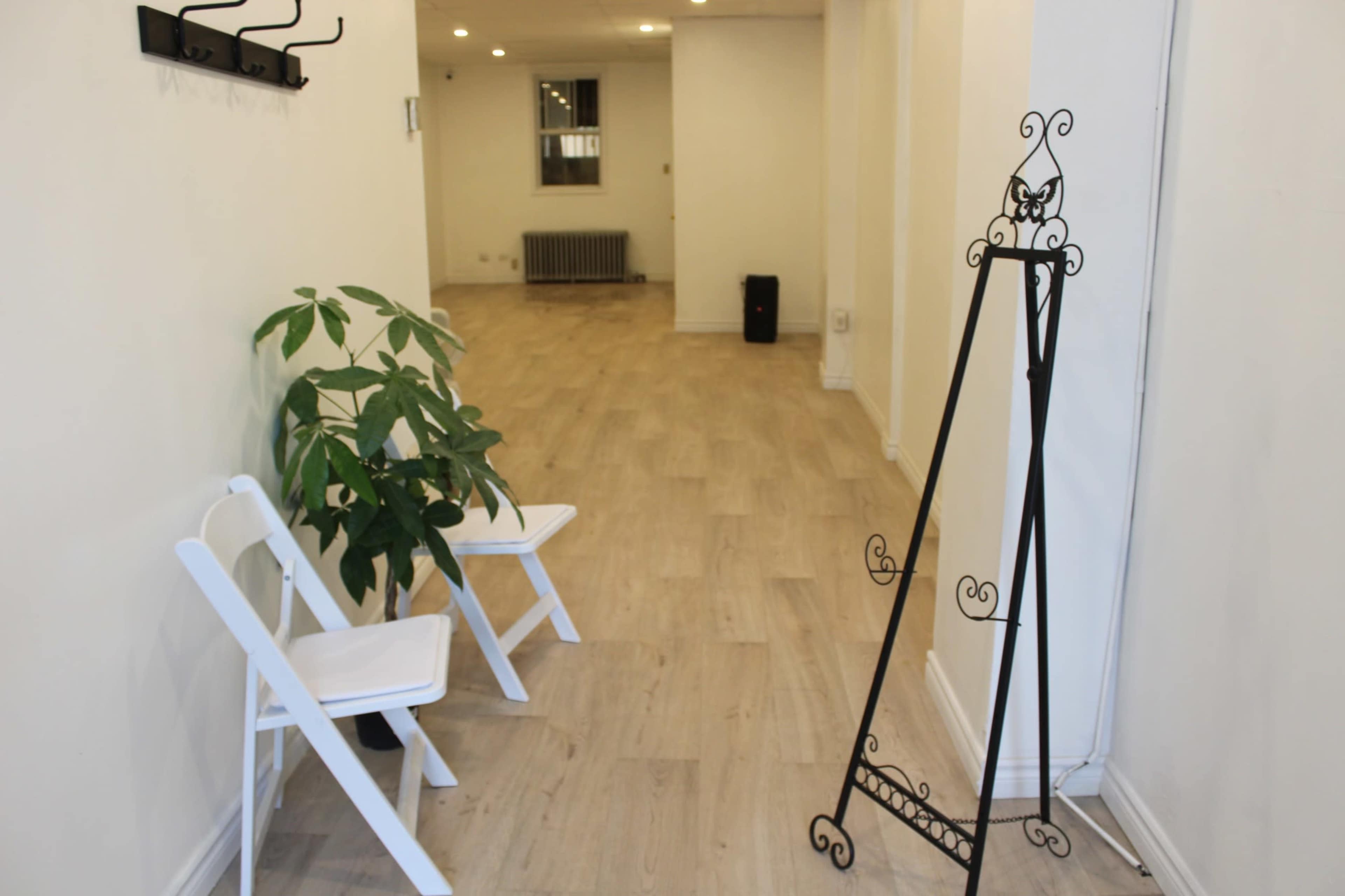 A narrow hallway featuring two white folding chairs, a potted plant, and a decorative metal stand against the wall.