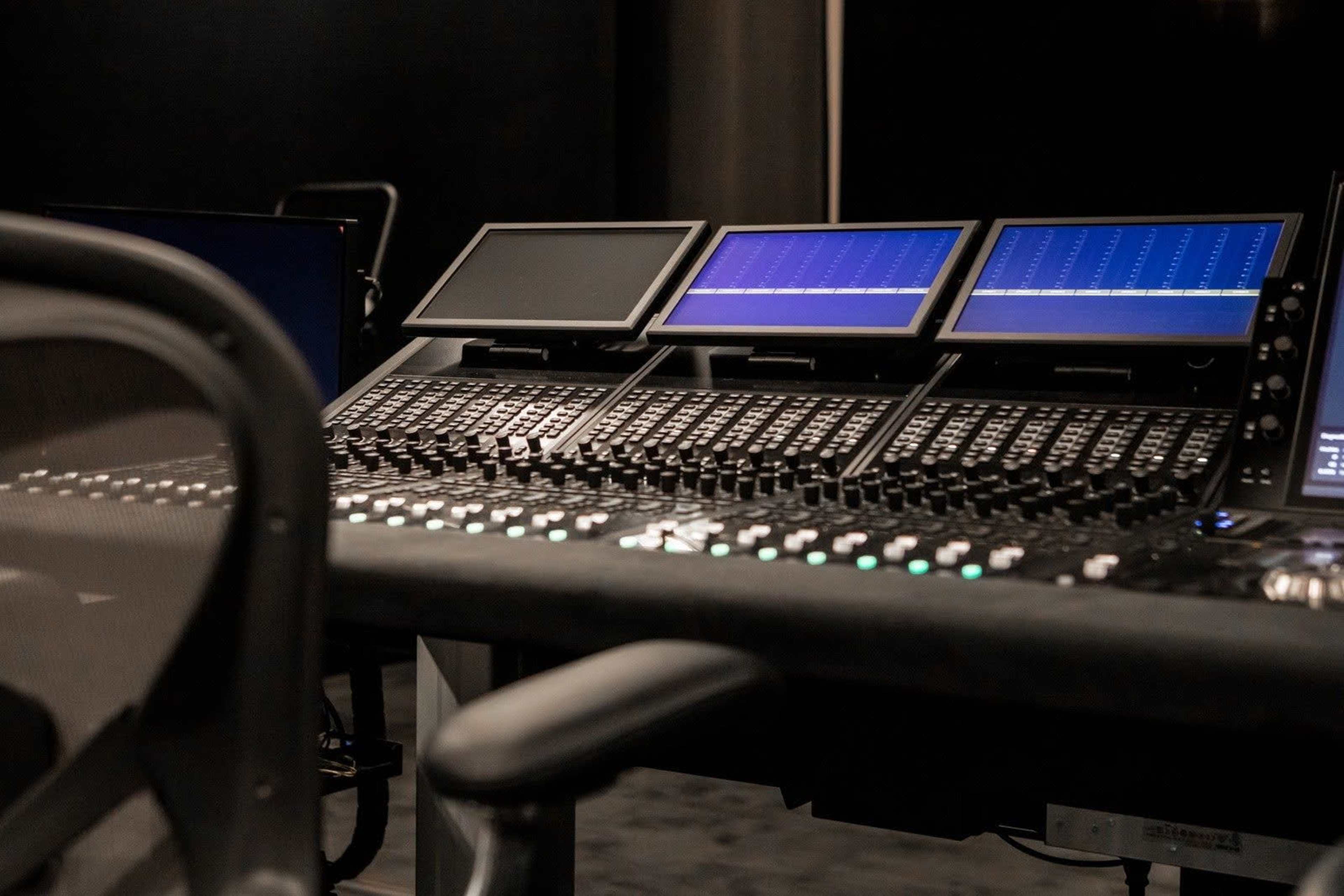 The image shows a close-up view of a sound mixing console with multiple screens and control panels.