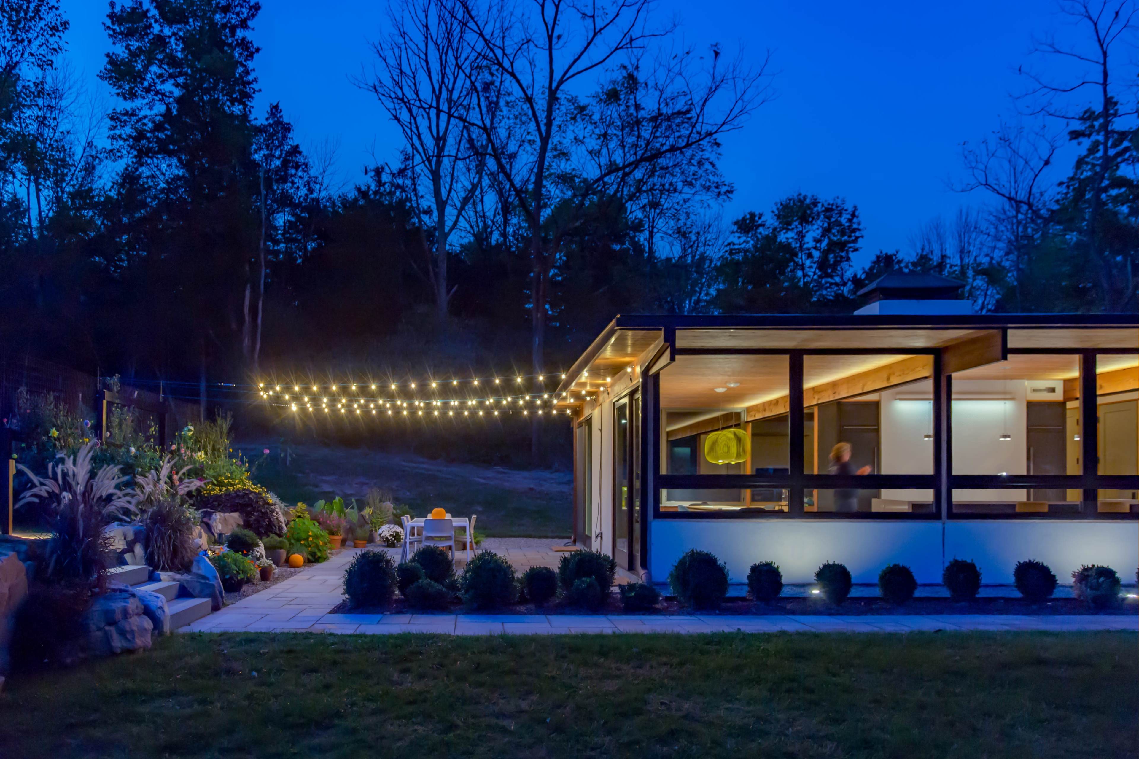 A modern house with outdoor string lights and a landscaped yard is set against a twilight sky.