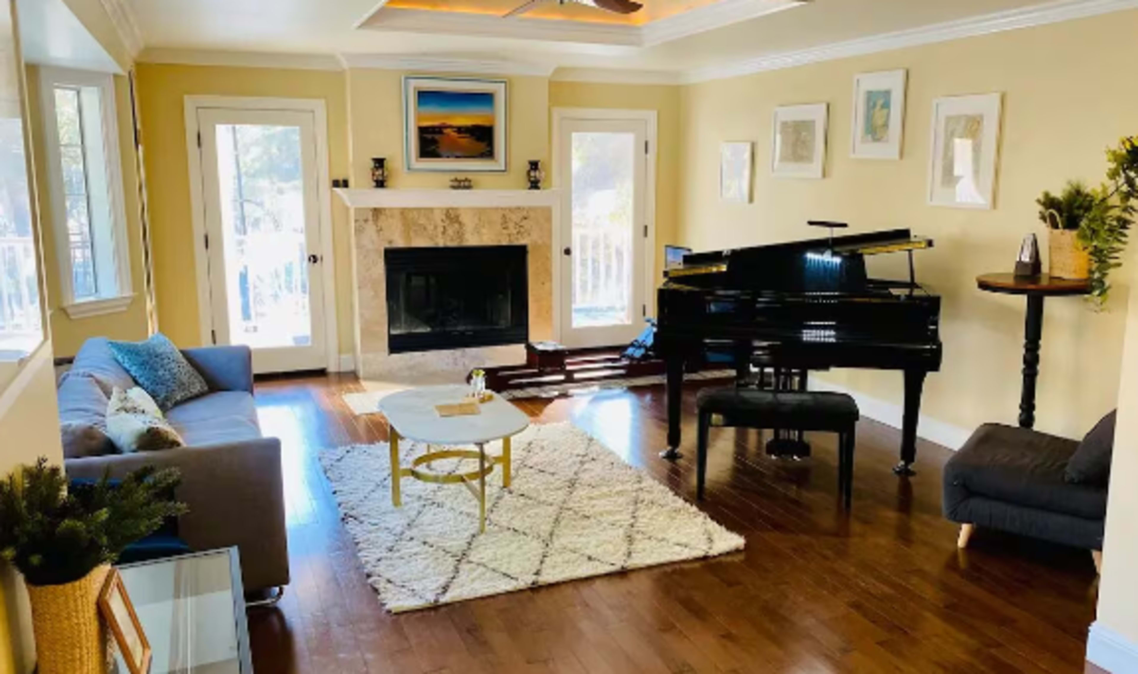 A modern living room features a grand piano, a fireplace, and large windows that let in natural light.