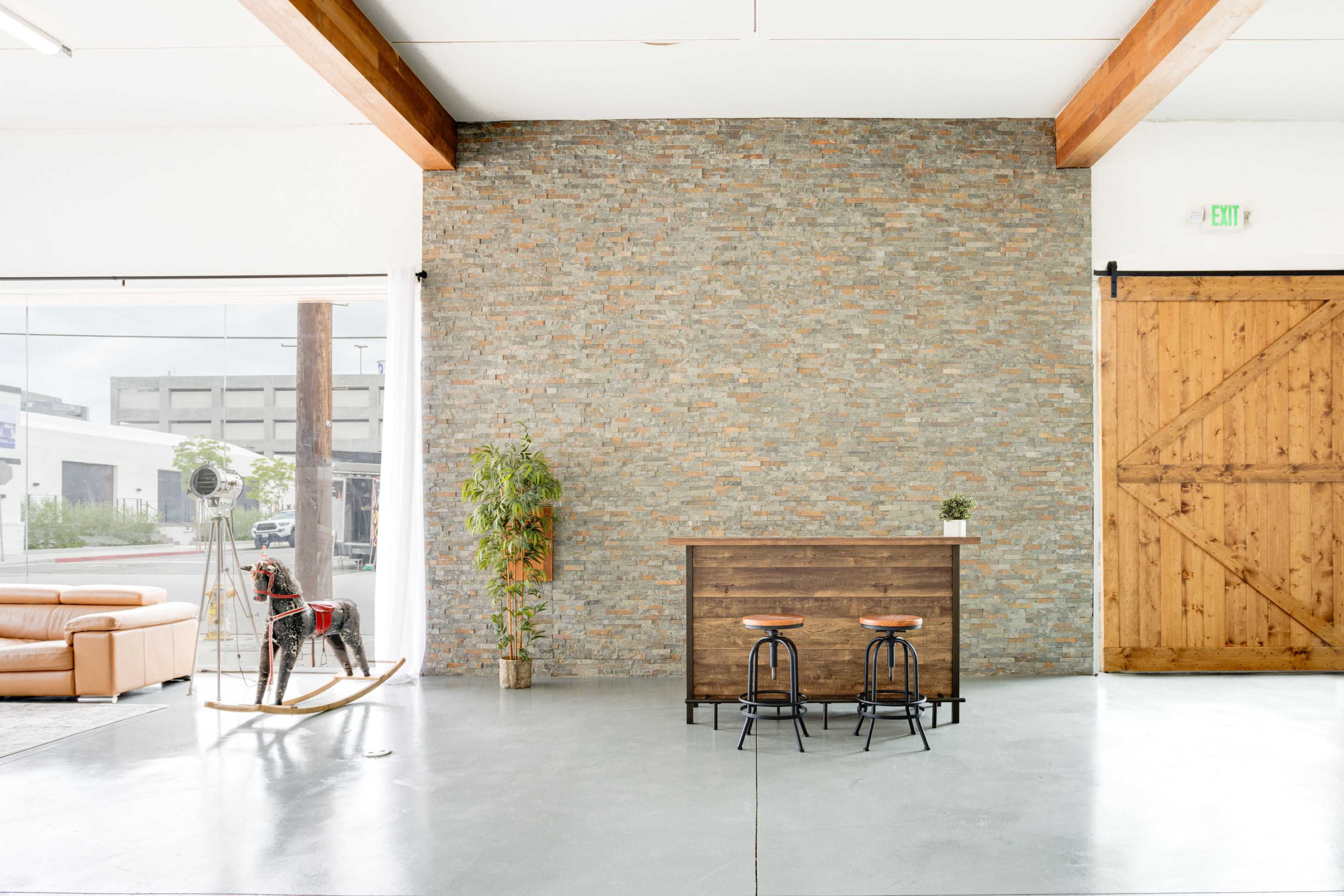 The scene features a spacious interior with a brick accent wall, a wooden bar with two stools, and a rocking horse near a large window.