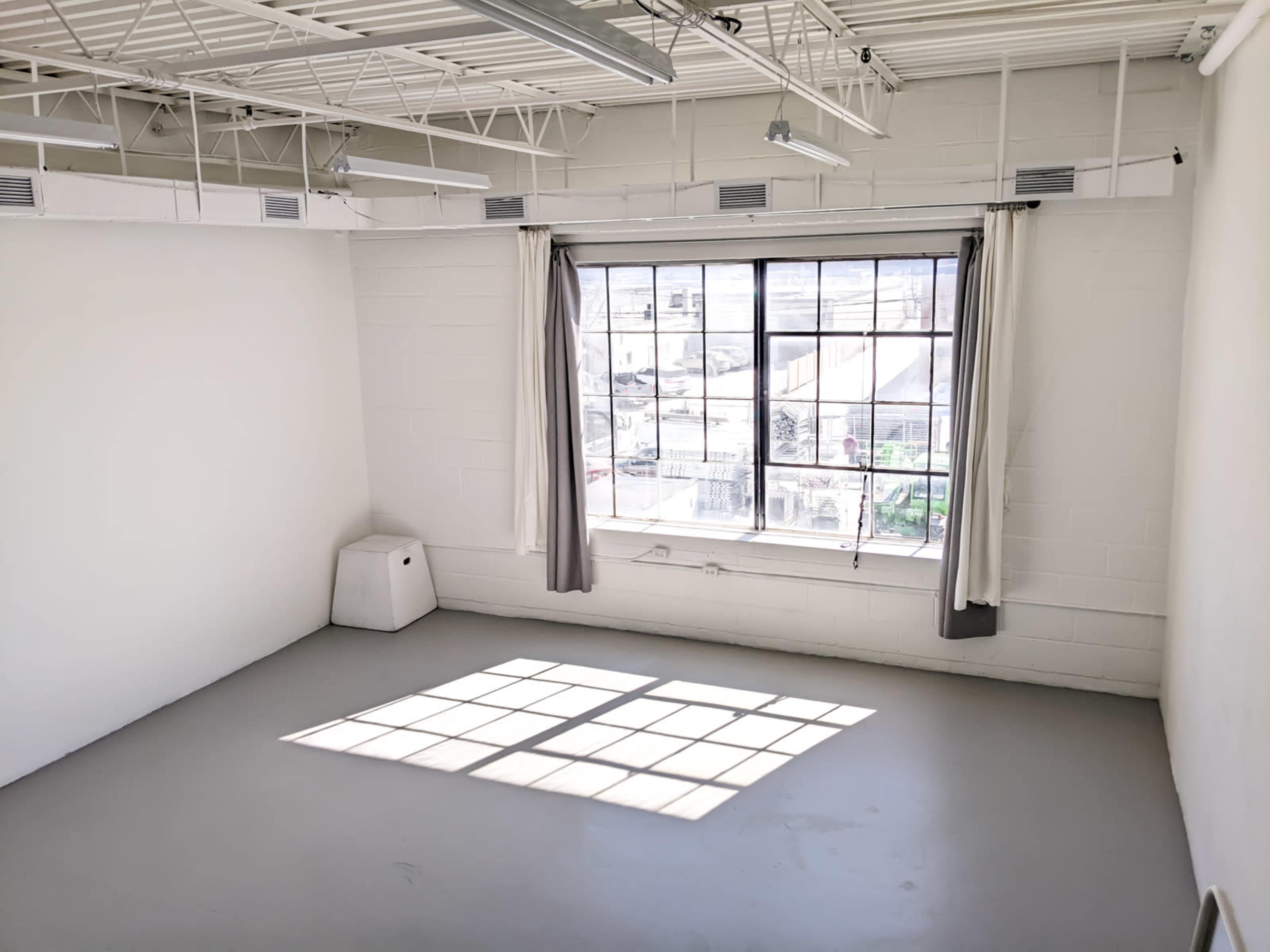 A bright, empty room features a large window with sunlight casting a shadow on the gray floor.