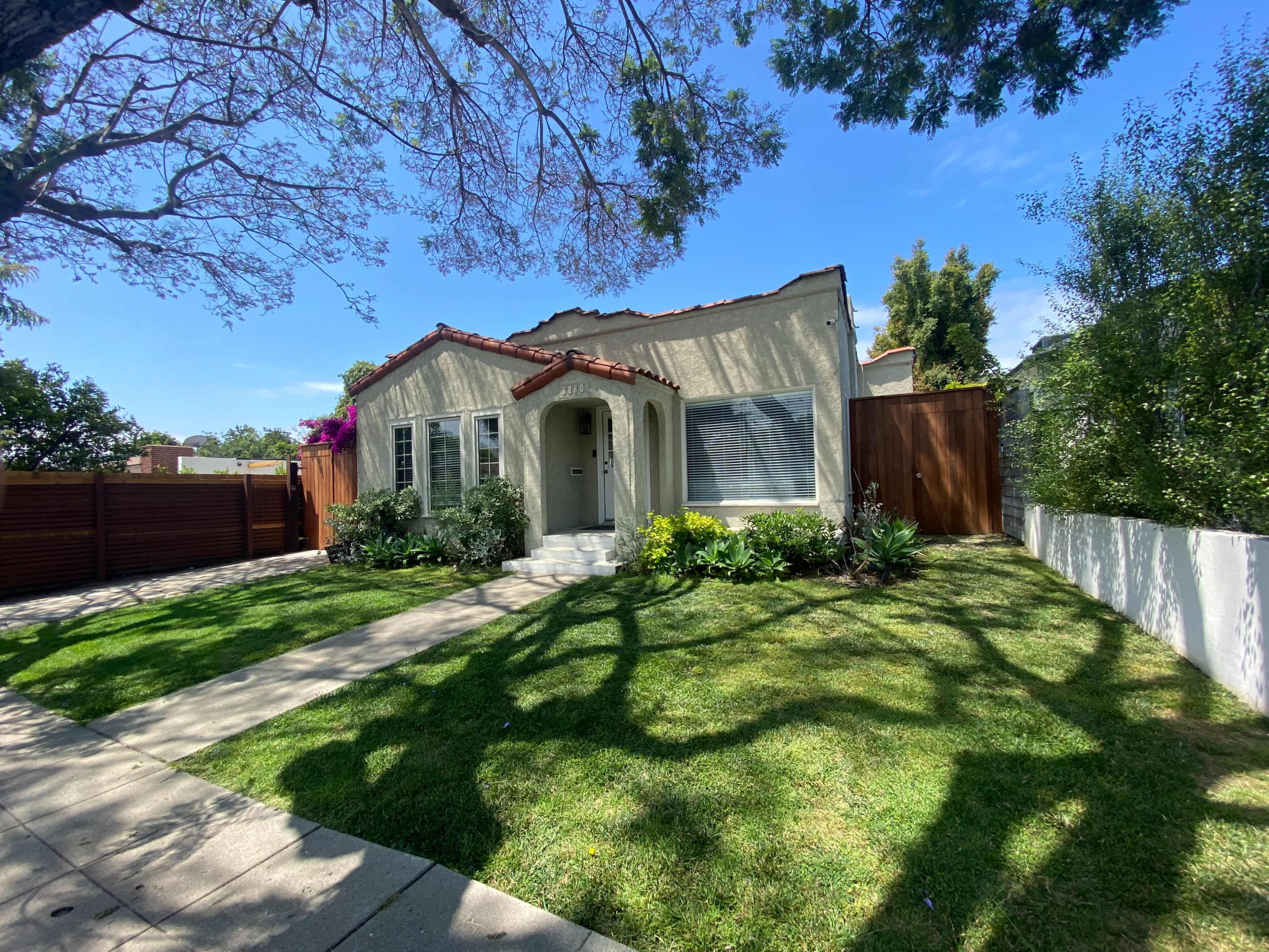A single-story house with a tiled roof and a front garden is set against a blue sky.